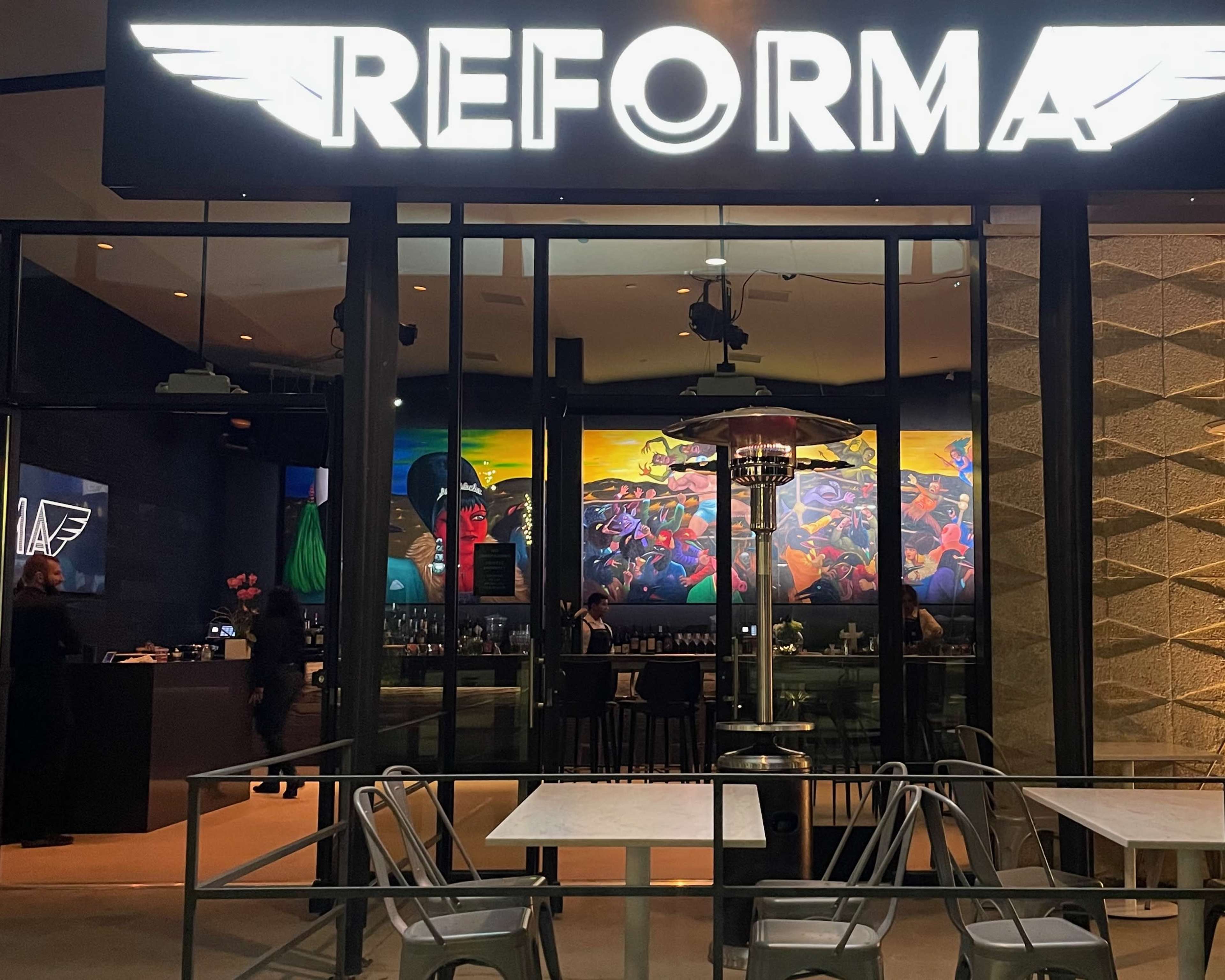 The image shows a restaurant named "REFORMA," featuring a colorful mural inside and outdoor seating with metal chairs and tables.