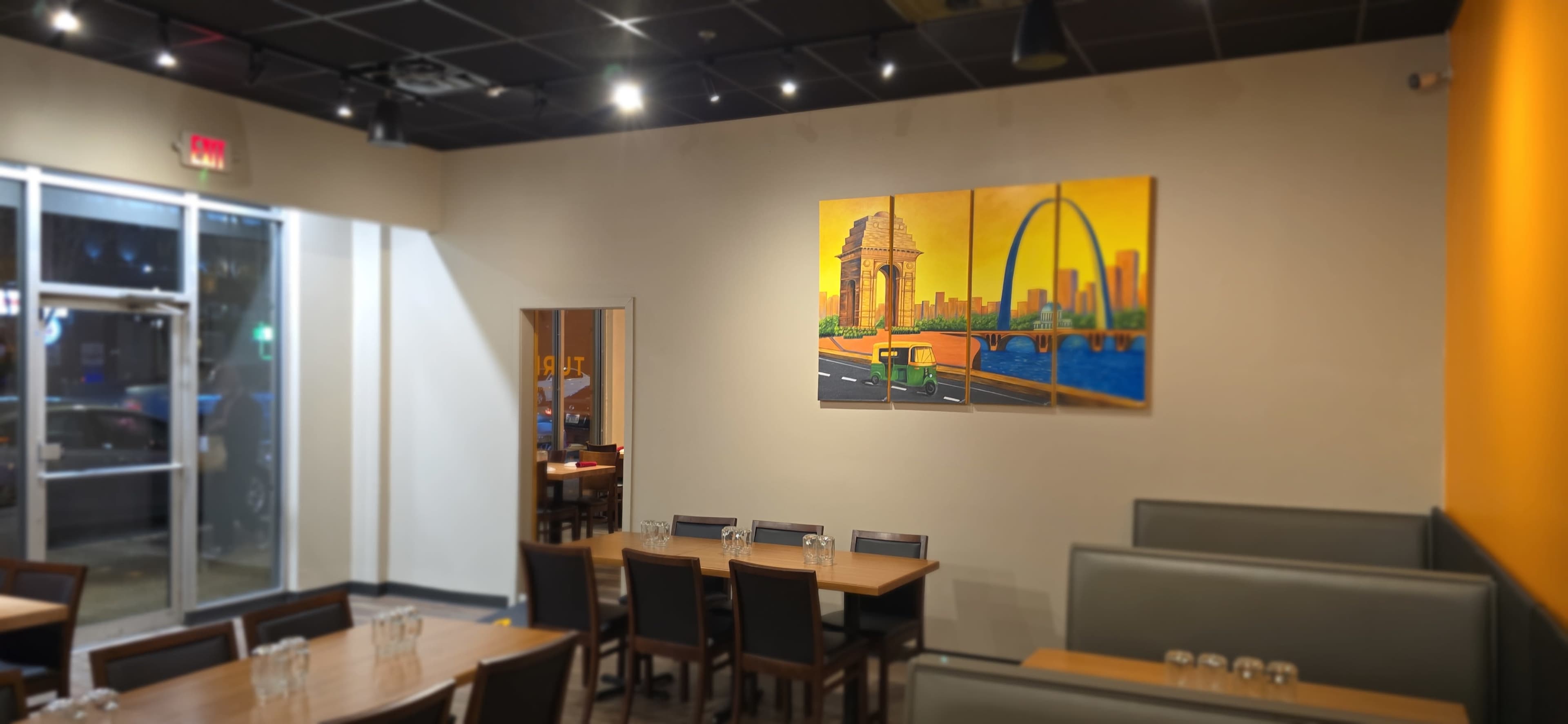 The image shows a restaurant interior with wooden tables, chairs, and a large mural depicting a city skyline on one wall.