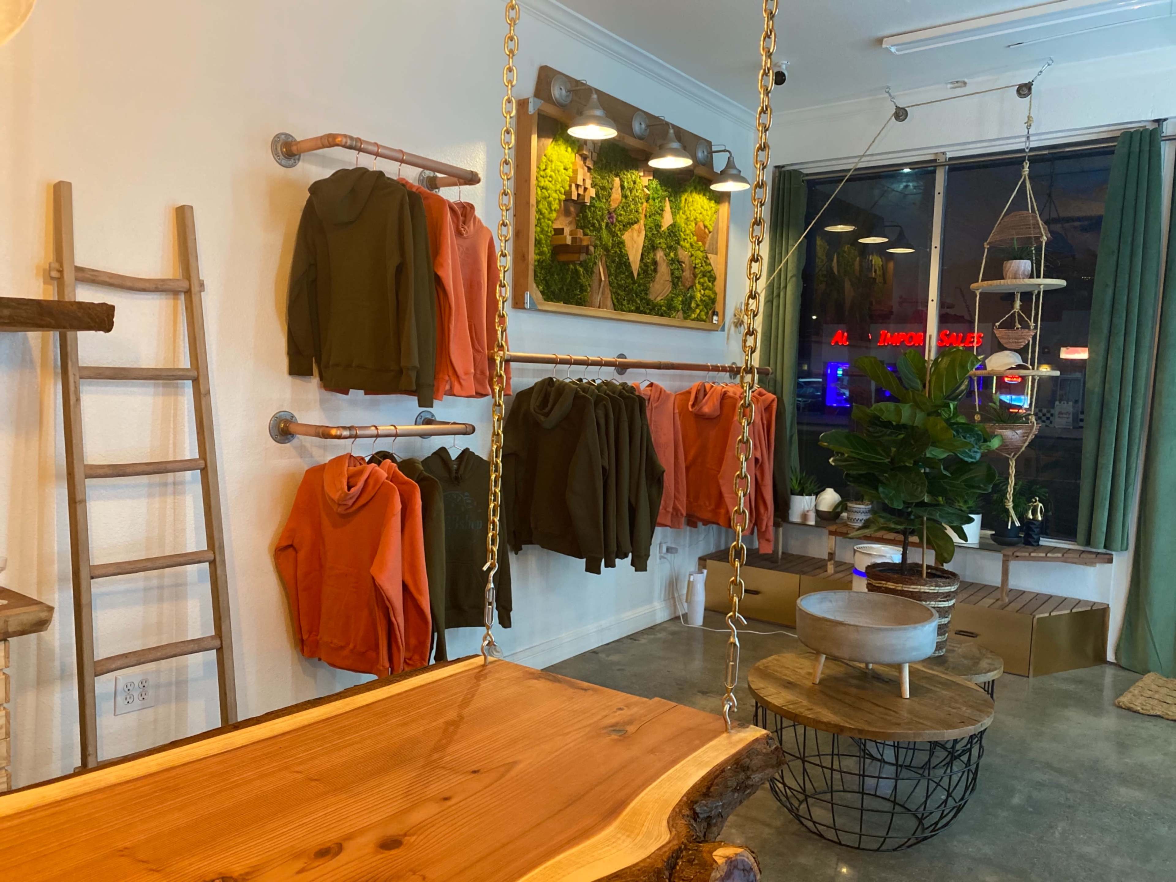A modern retail space with hanging clothing racks displaying hoodies, a wooden table, and decorative plants.