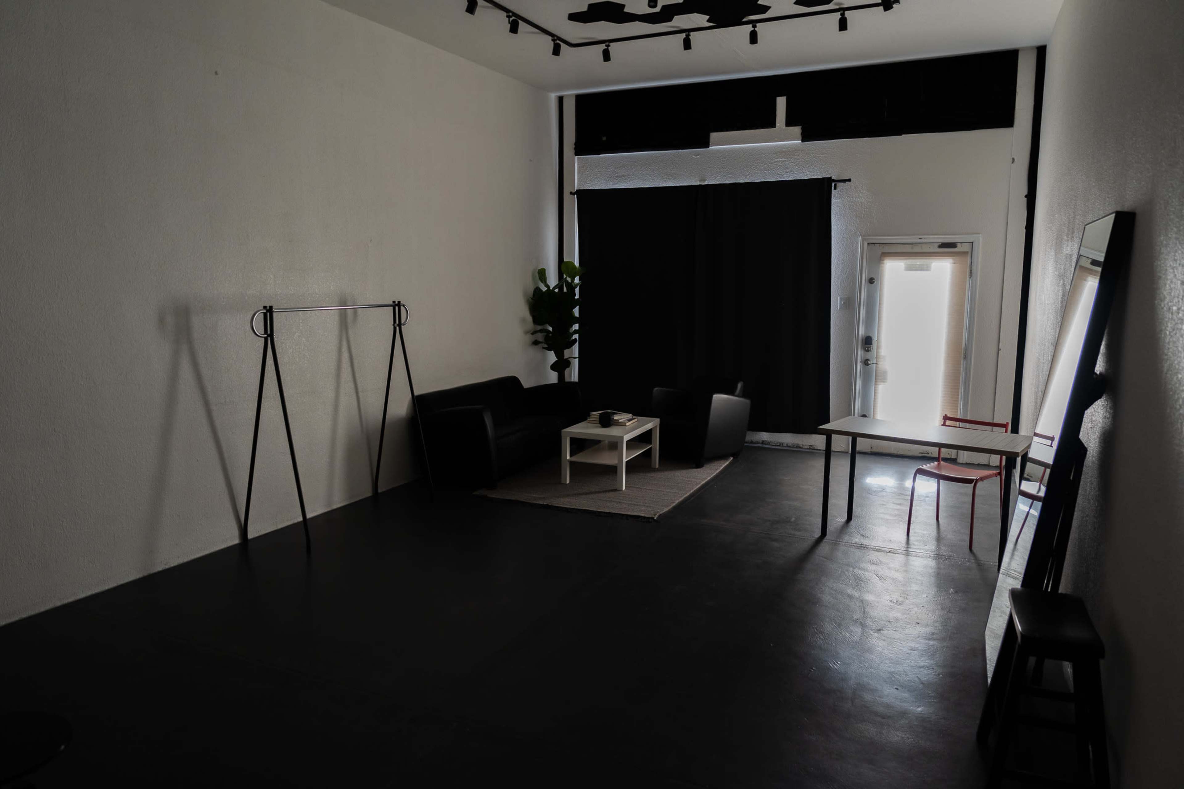 A spacious, minimally furnished room with a black curtain, a sofa set, a coffee table, and a door leading outside.