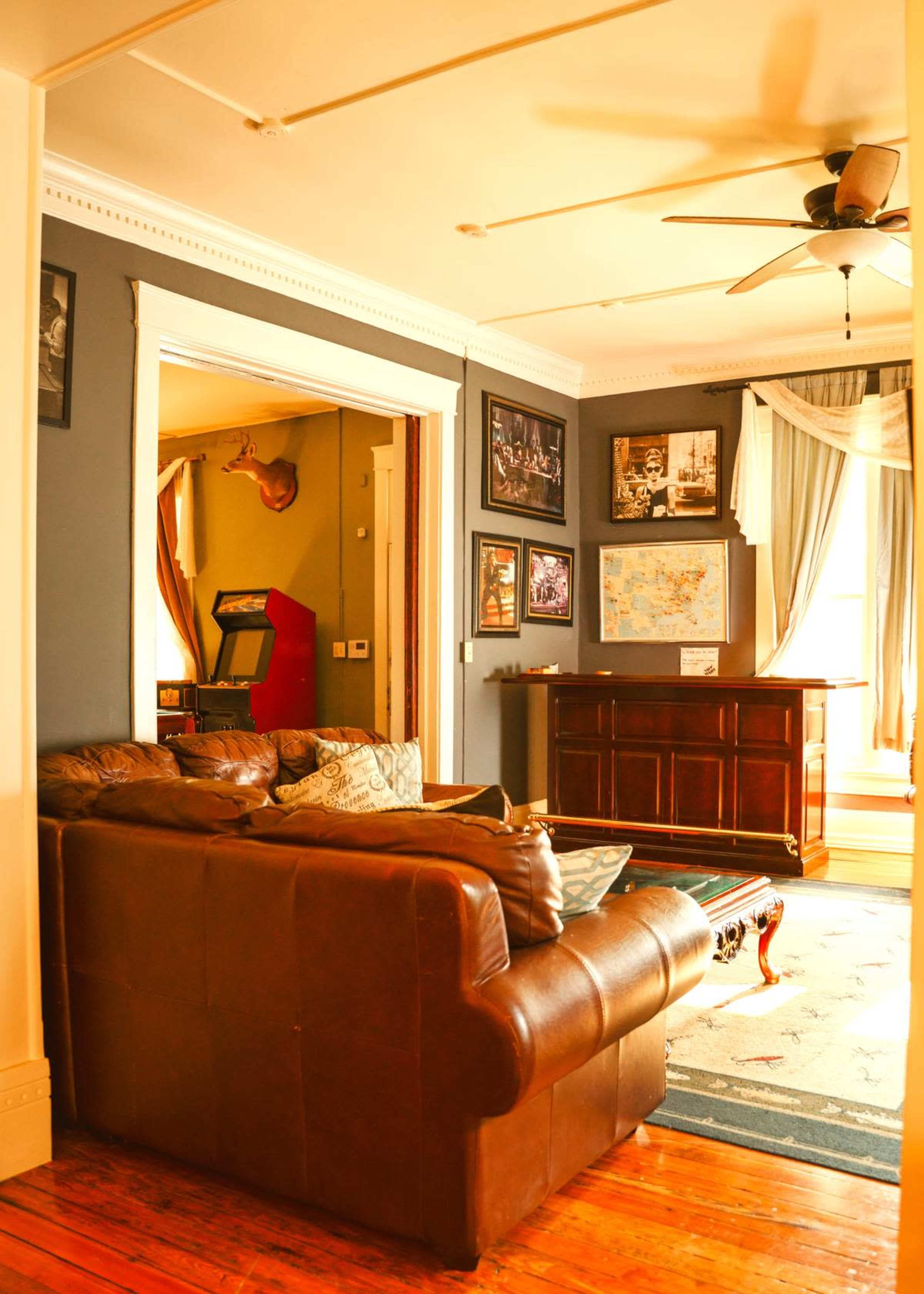 The image shows a cozy living room with a brown leather couch, framed photographs on the walls, and a wooden bar cabinet in the corner.