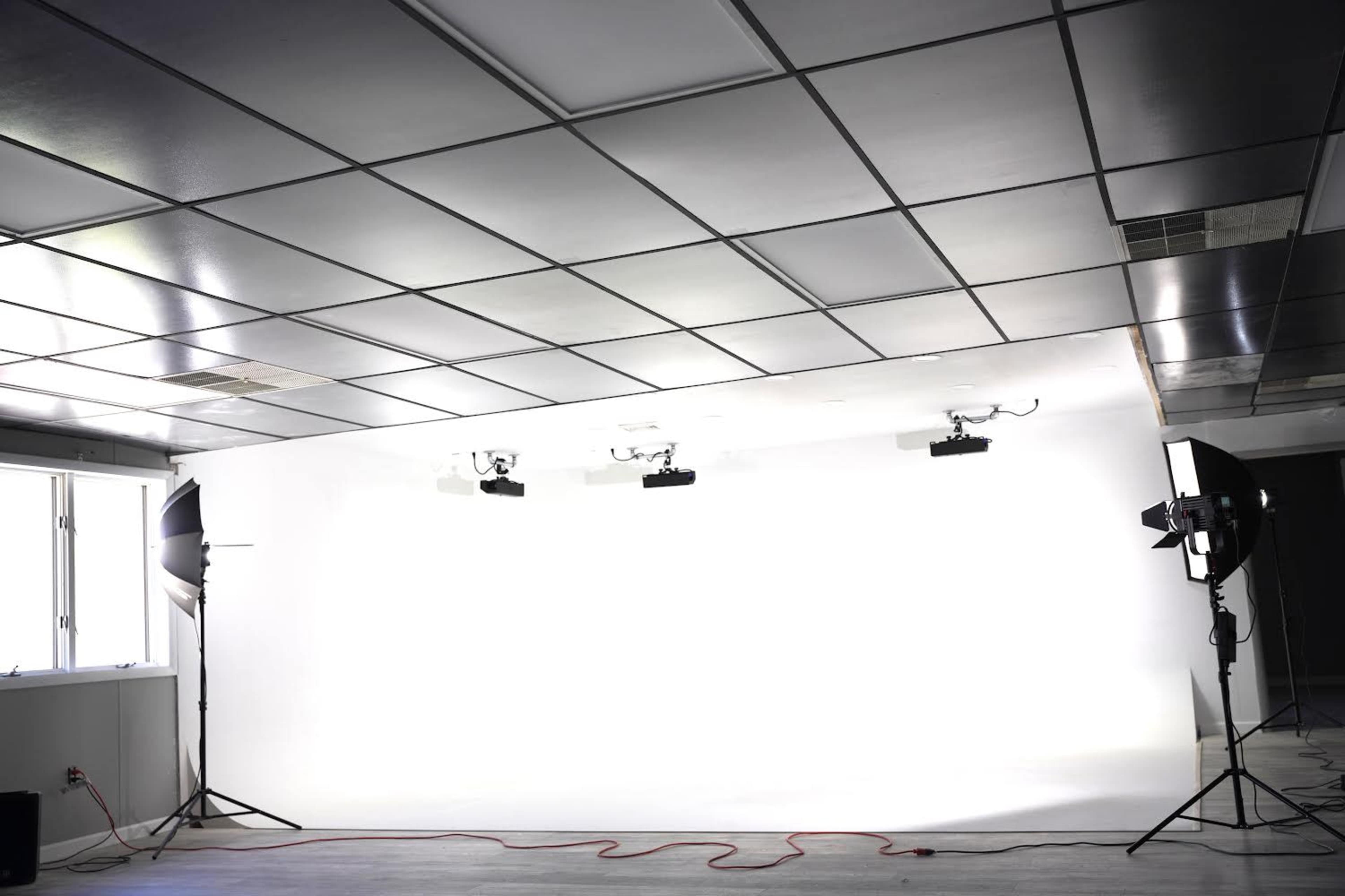 A photo studio with a bright white backdrop and three lighting setups positioned on either side.