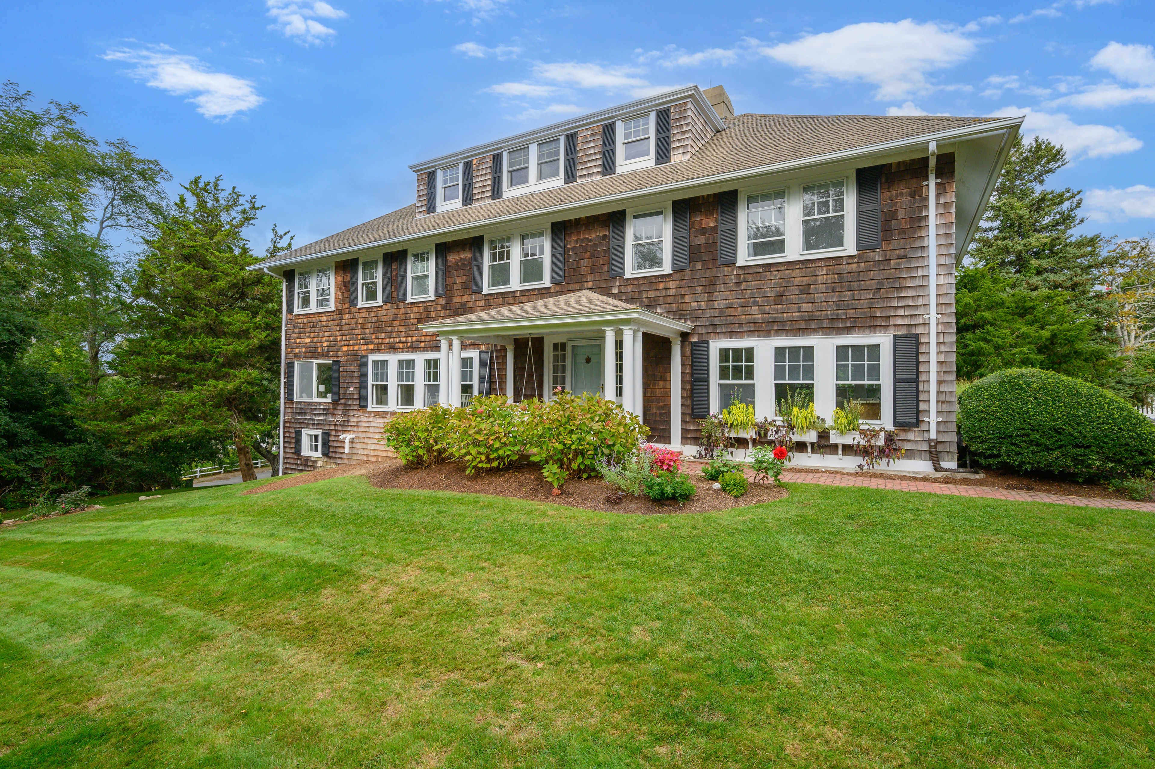 A large, two-story house with a wooden exterior, surrounded by a well-maintained lawn and shrubs.
