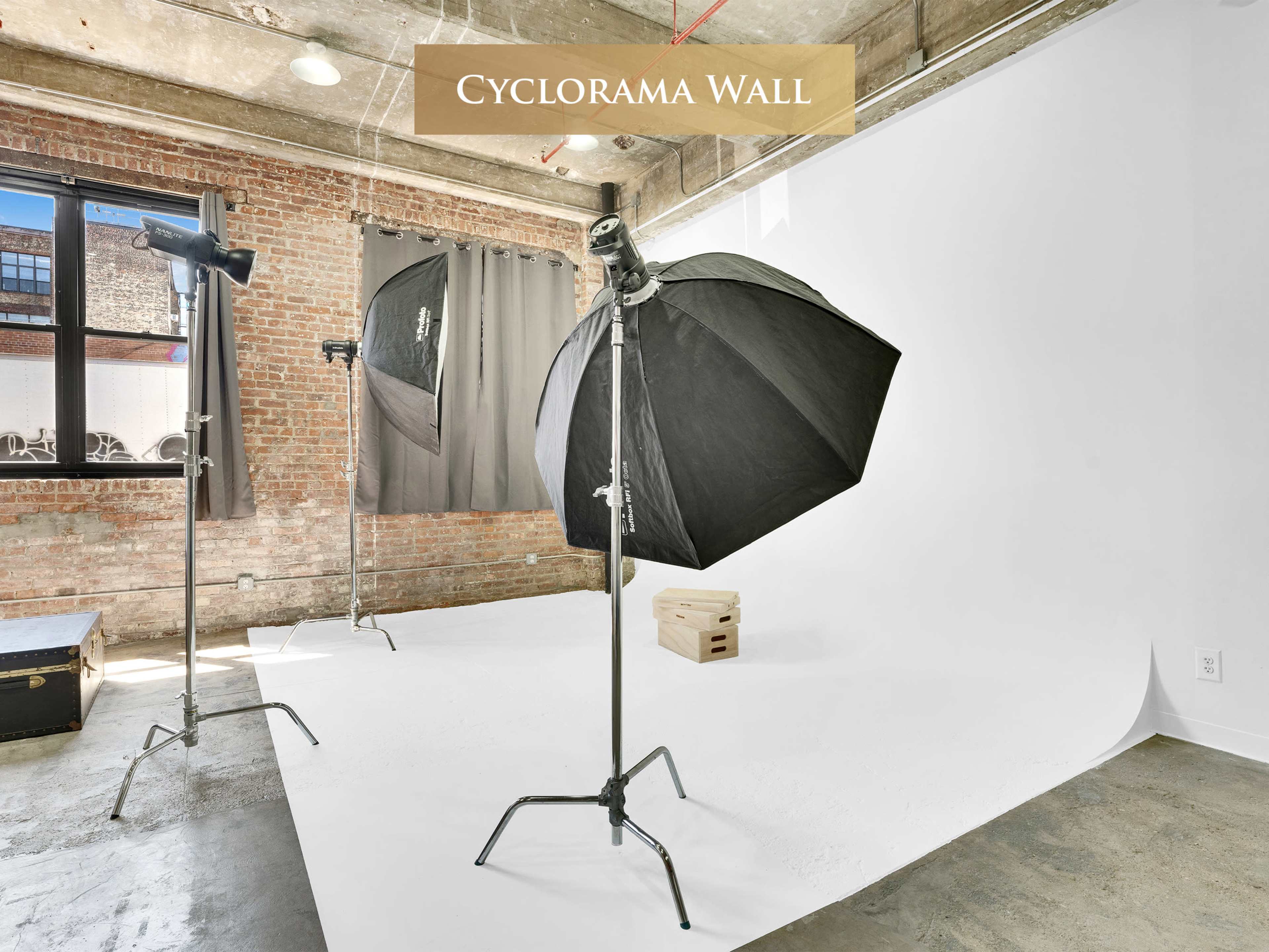 The image shows a photography studio with a cyclorama wall, featuring two softbox lights on stands and a wooden crate on a white backdrop.