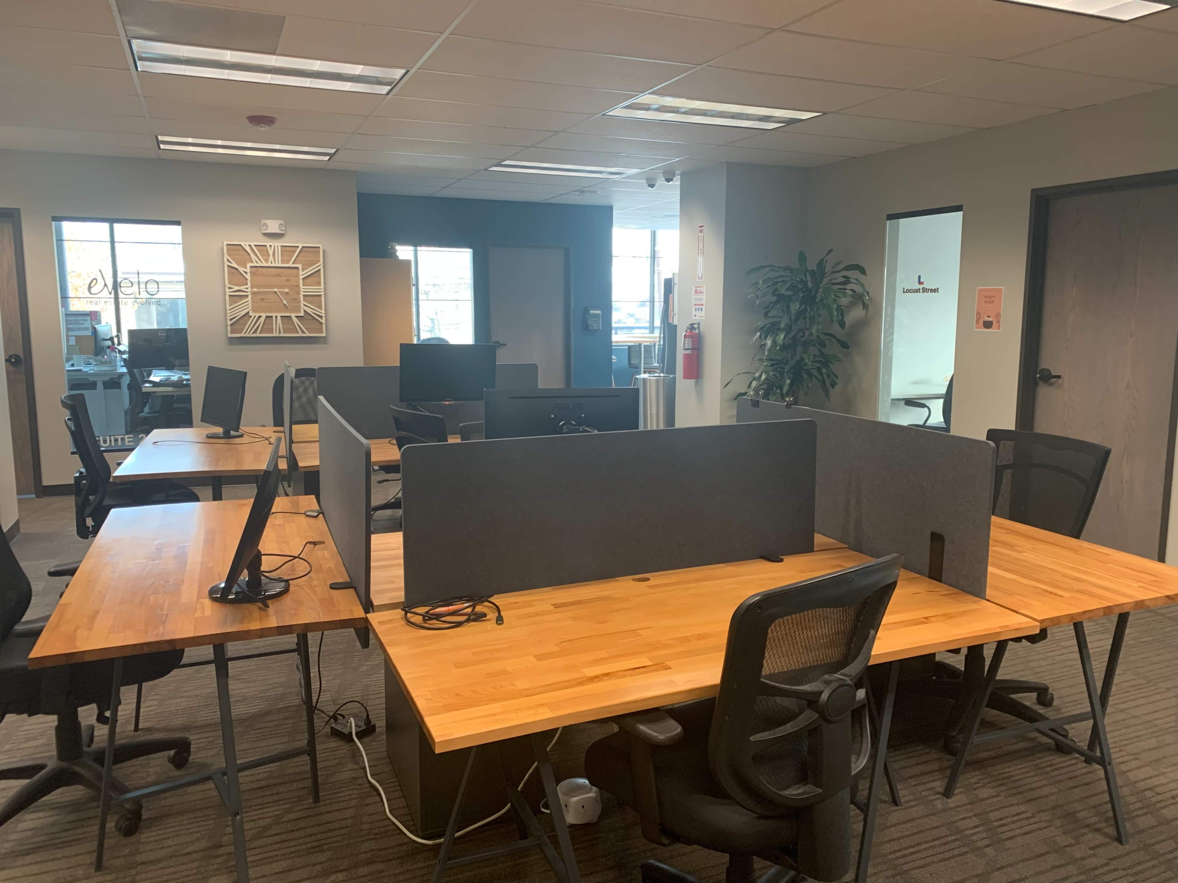 An office space with several workstations featuring wooden desks and ergonomic chairs, separated by gray partition walls.