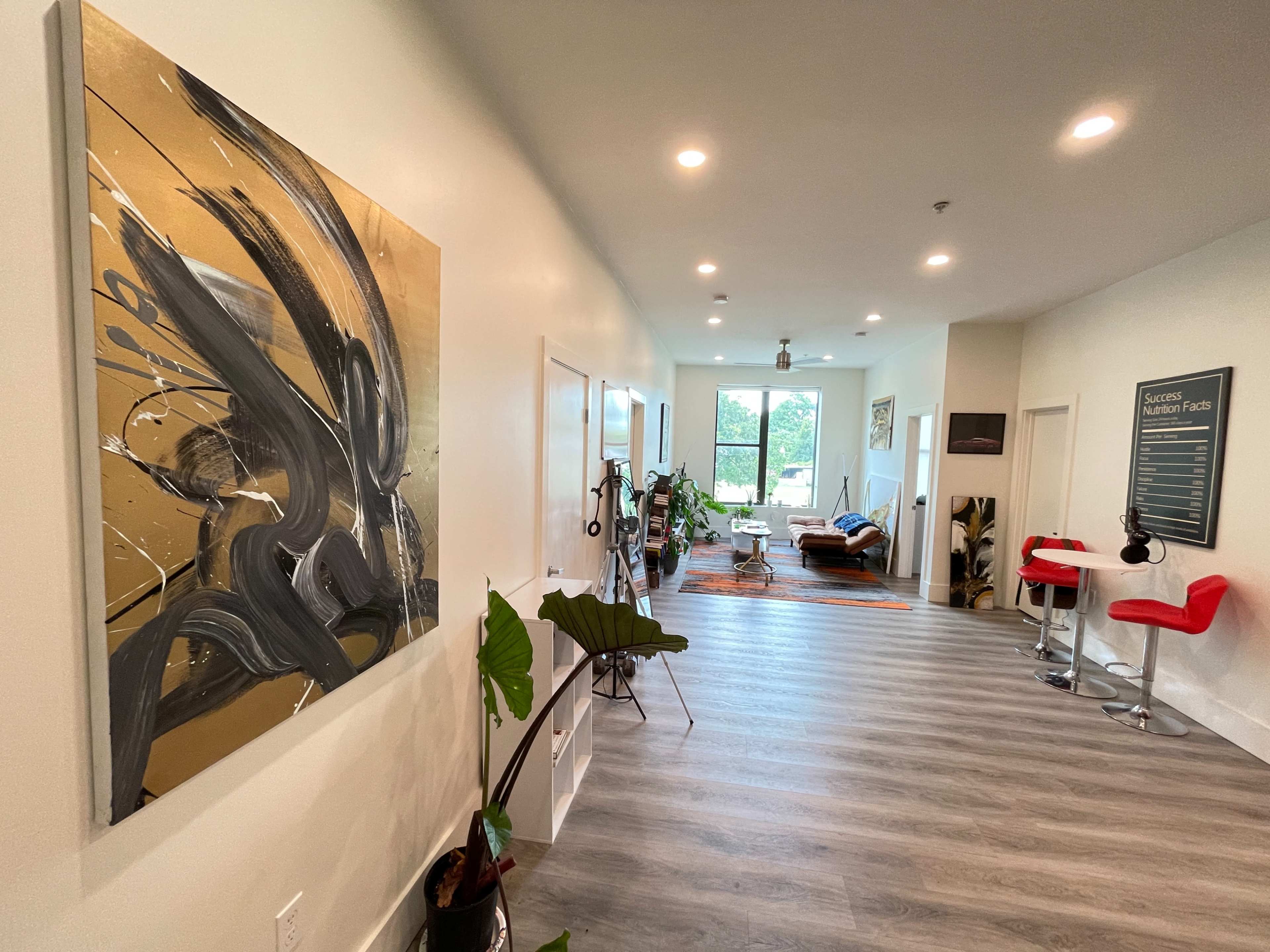 A long hallway leading to a bright room with artwork on one wall, plants, and a mix of modern furniture.