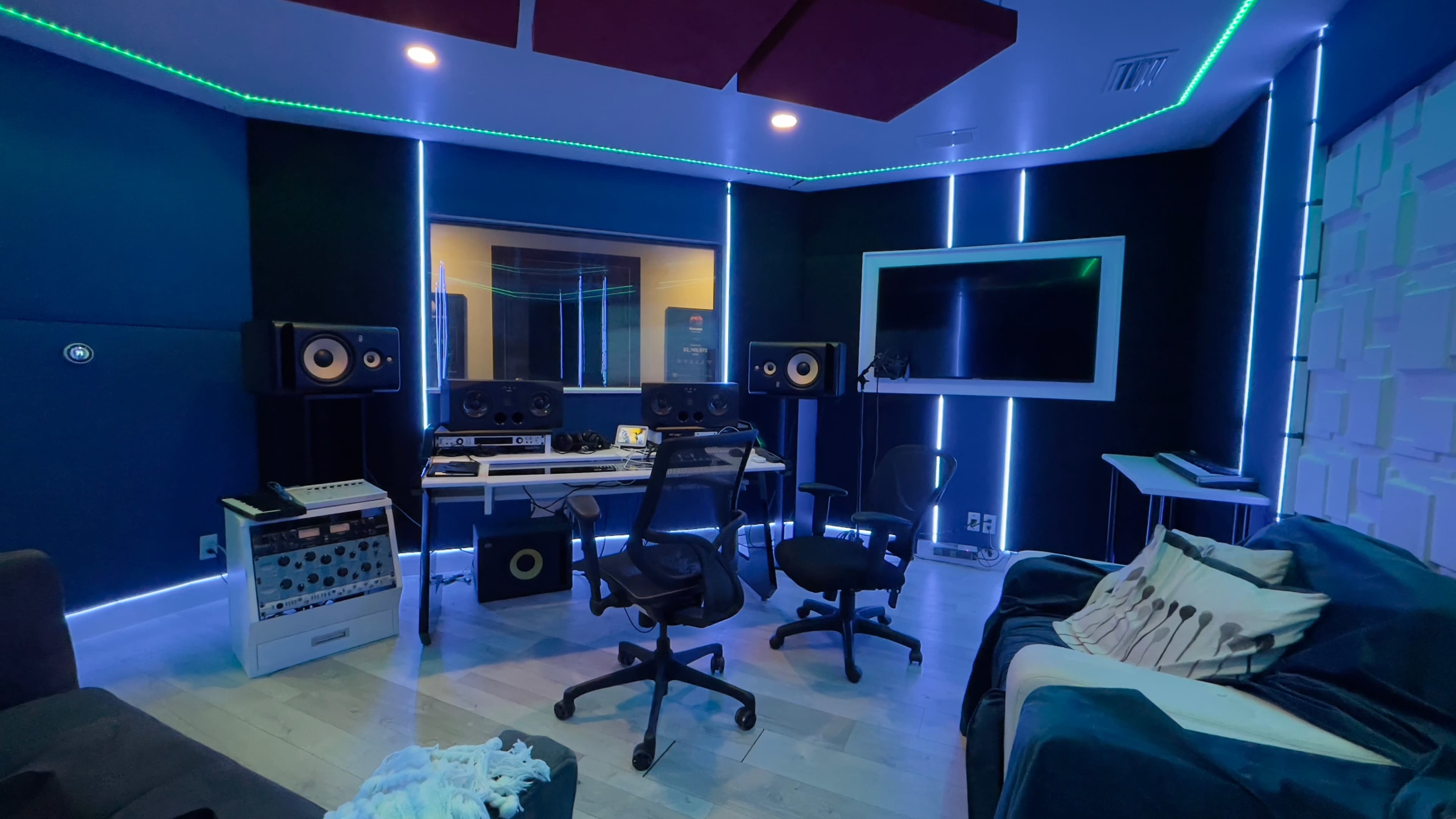 A modern recording studio with two chairs, audio equipment, and blue LED lighting along the walls.