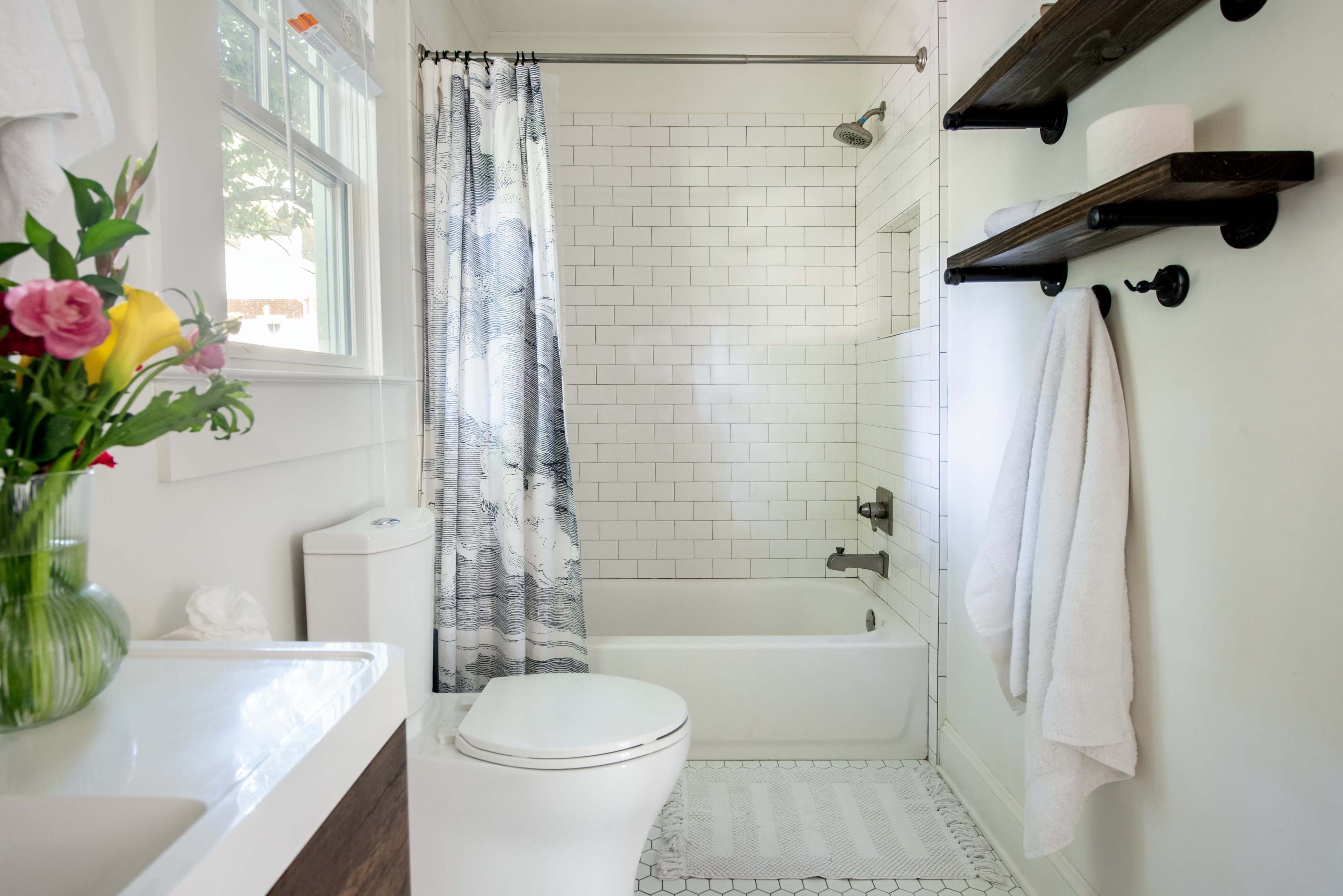 A neatly arranged bathroom featuring a white tiled shower, a bathtub, a toilet, and a vase of flowers on the sink.