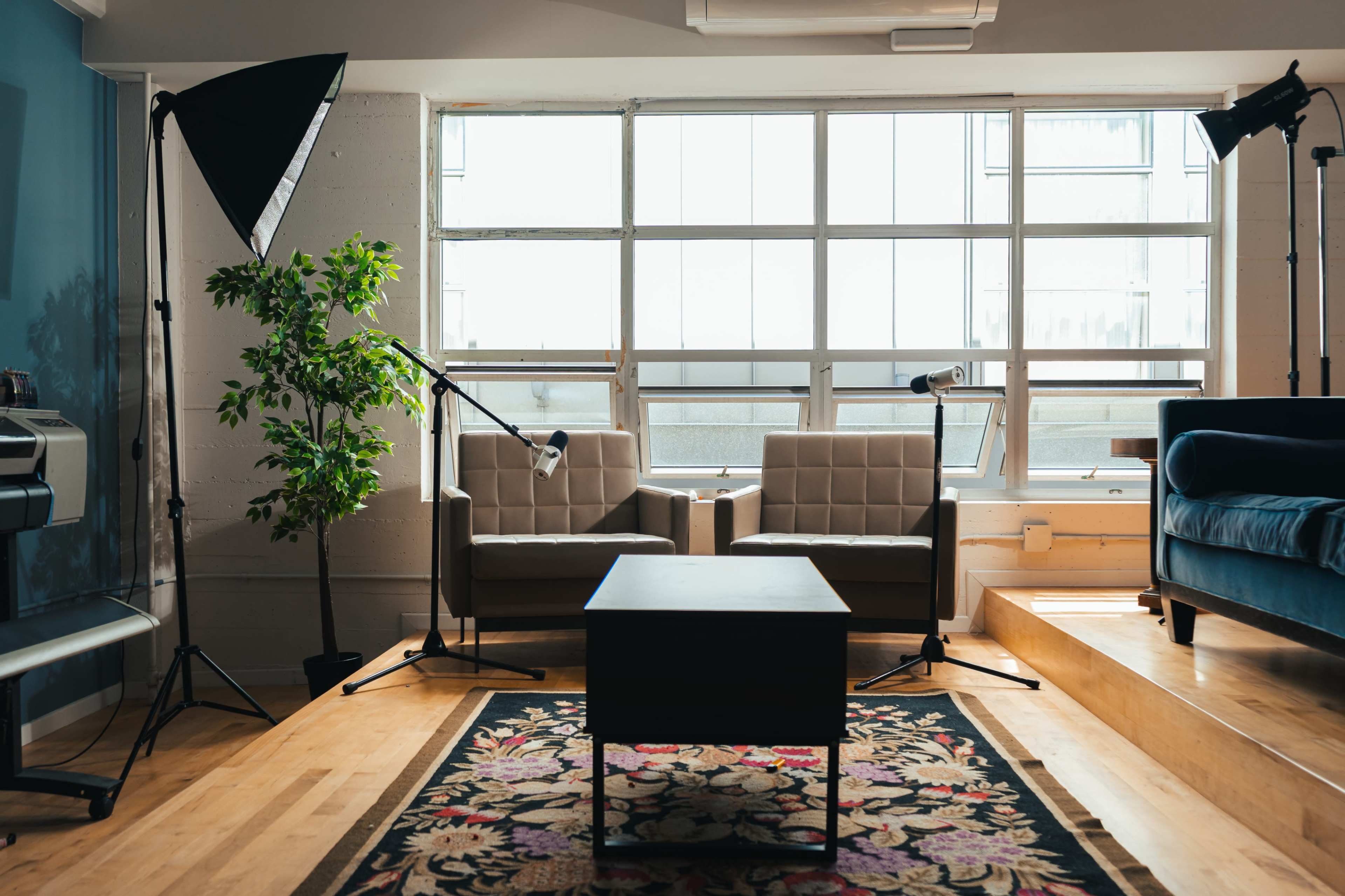 A well-lit interior space featuring two armchairs, a coffee table on a patterned rug, and a large window illuminating the area.