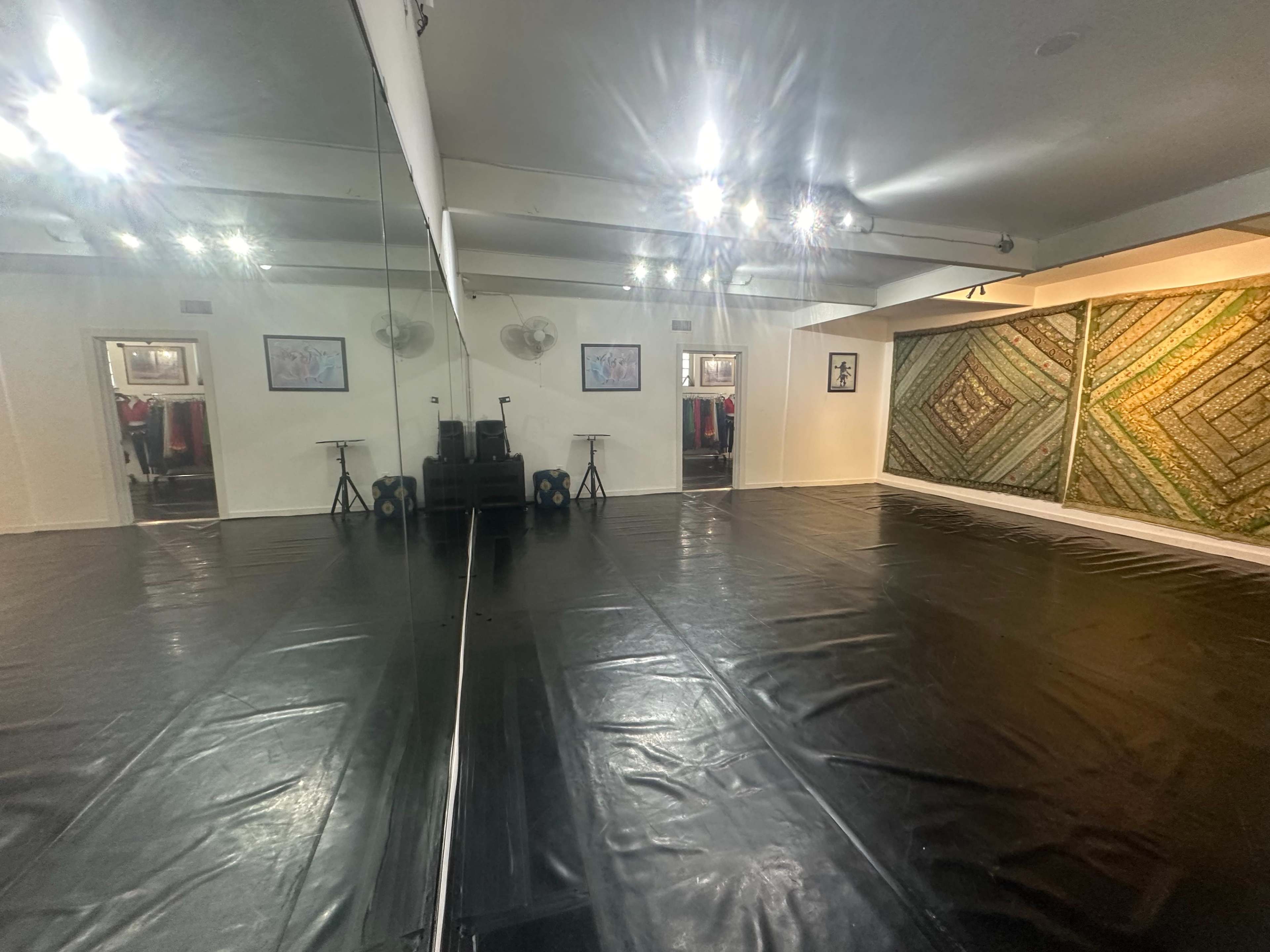The image shows a spacious indoor studio with mirrored walls, a black floor covering, and decorative artwork on one side.