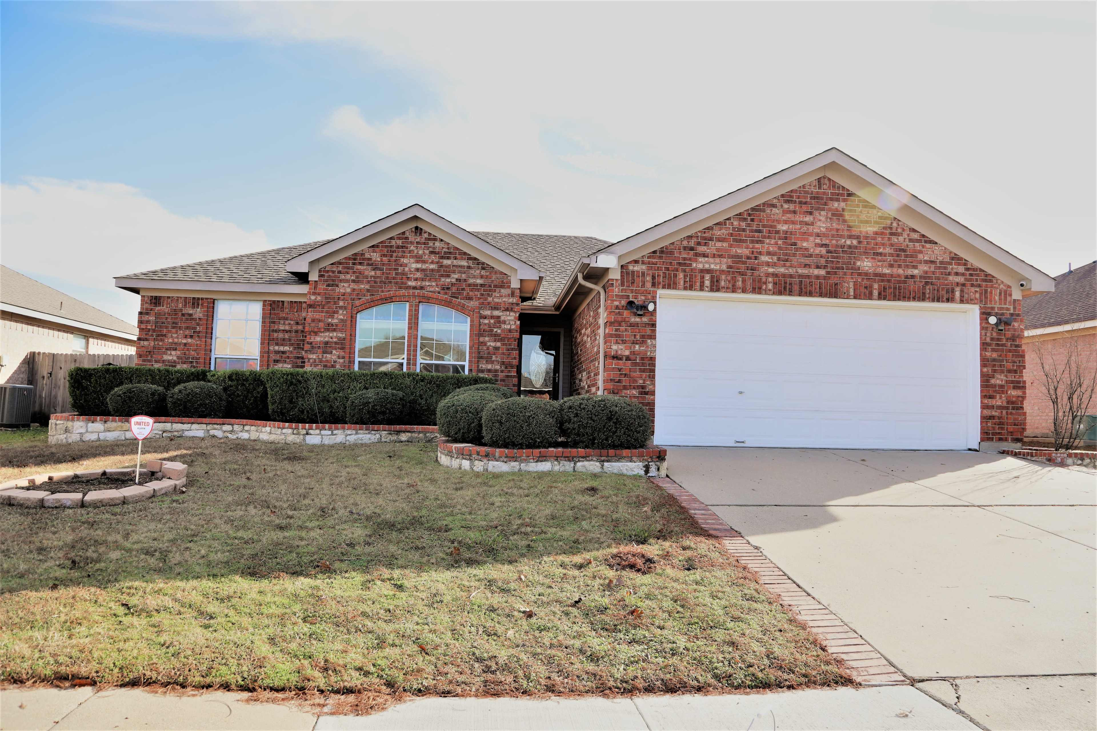 A single-story brick house with a large front yard, a circular stone garden, and a two-car garage.