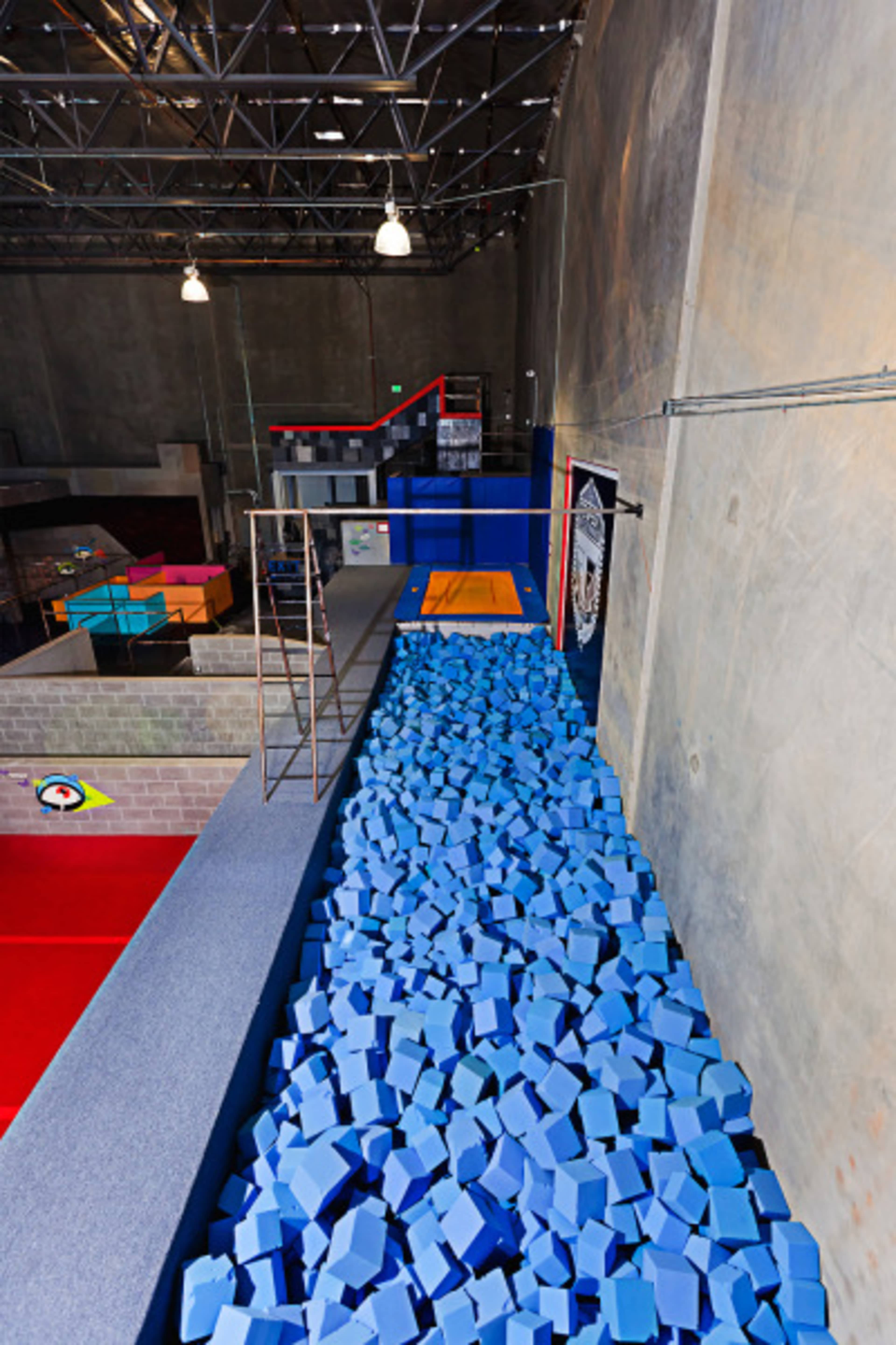 A foam pit filled with blue foam cubes, located inside a gym with various climbing and jumping apparatuses.