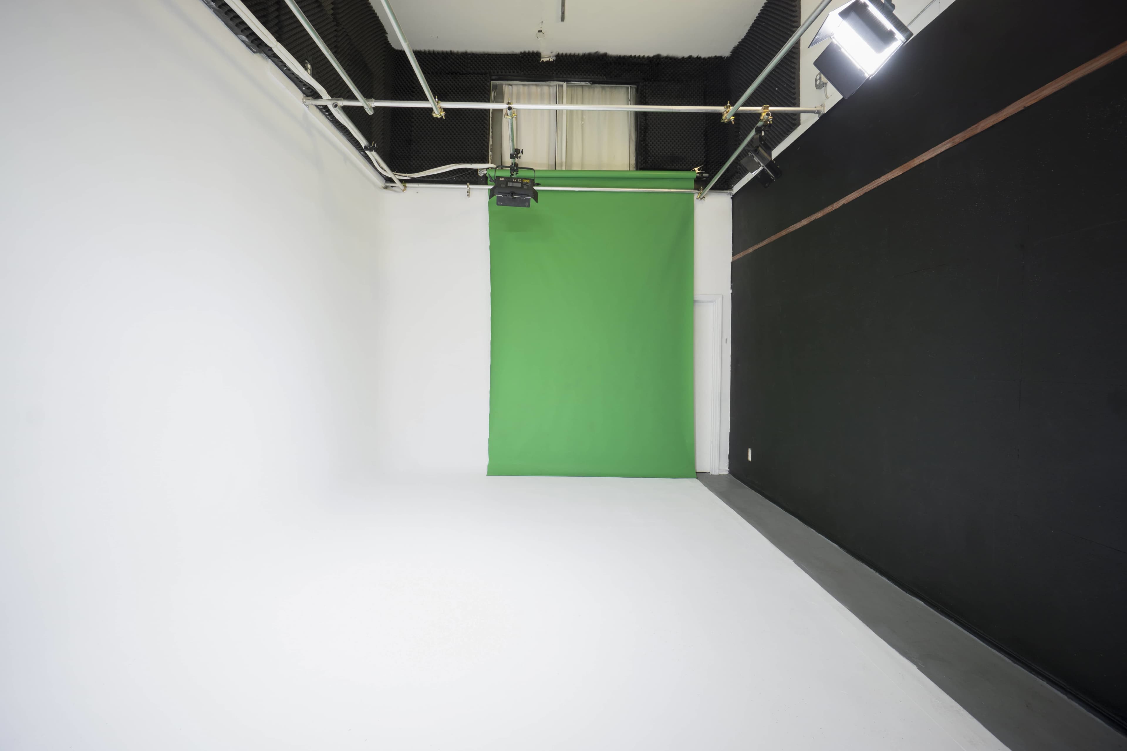 A photography studio with a green backdrop in the center and white walls on one side.