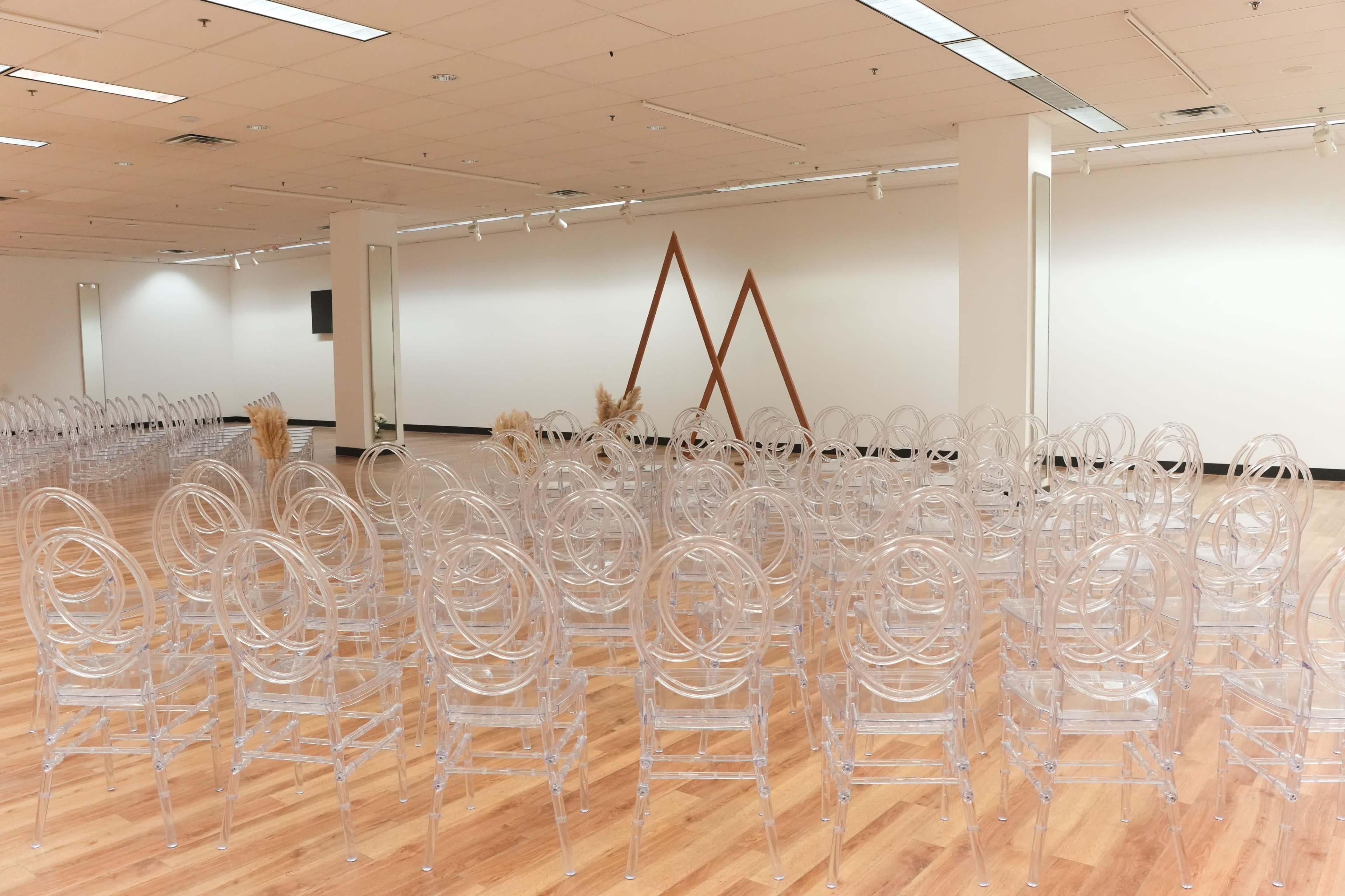 A spacious room is set up with clear acrylic chairs arranged in rows facing a wooden geometric structure on the wall.