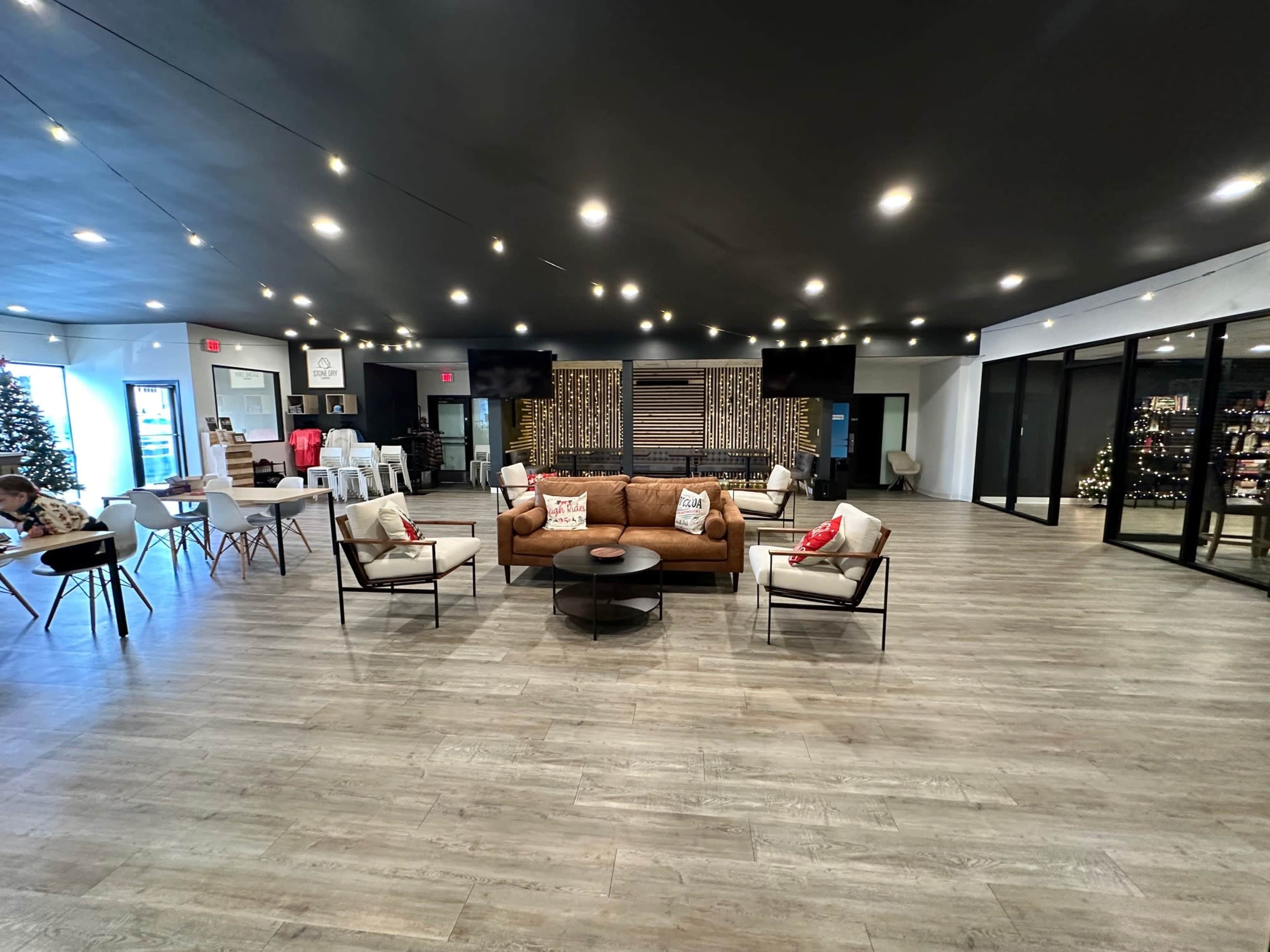 The interior of a modern event space features a brown sofa, white chairs, tables, and decorative lights.