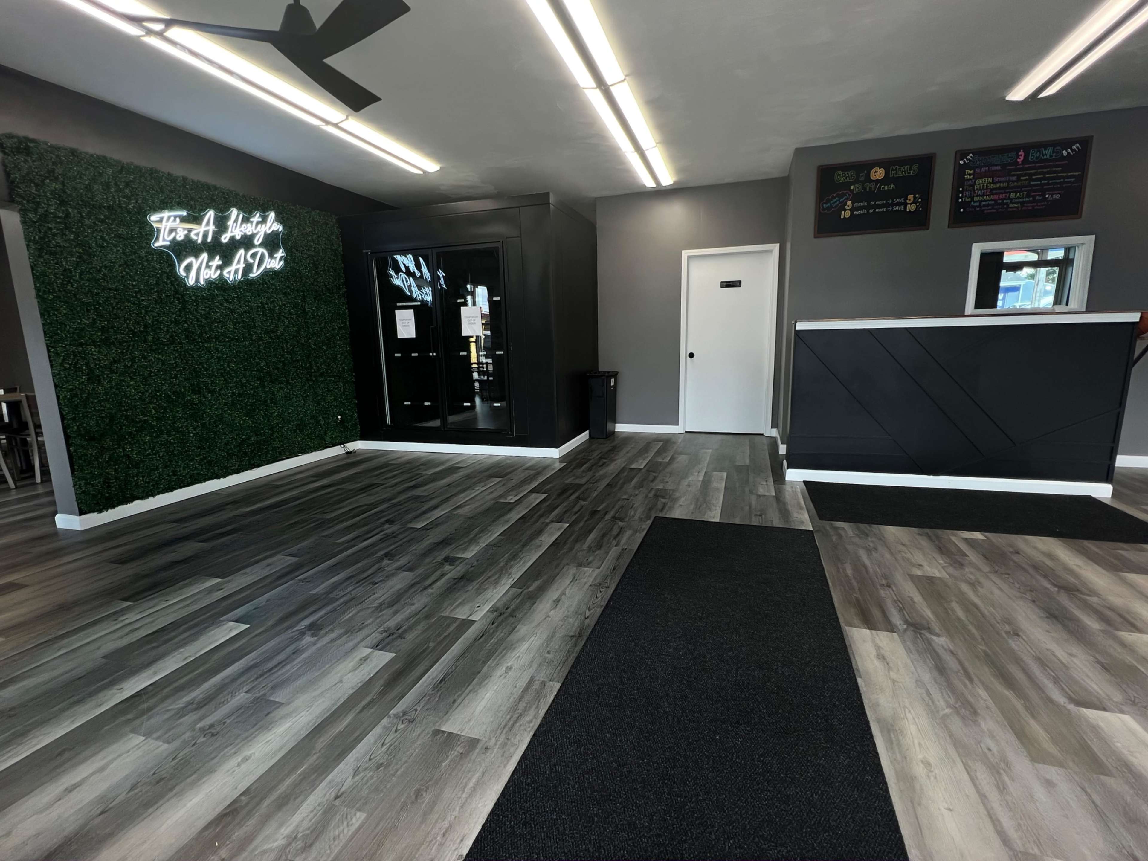 A spacious interior with a reception area featuring a dark counter, green accent wall with decorative lighting, and a large open floor.