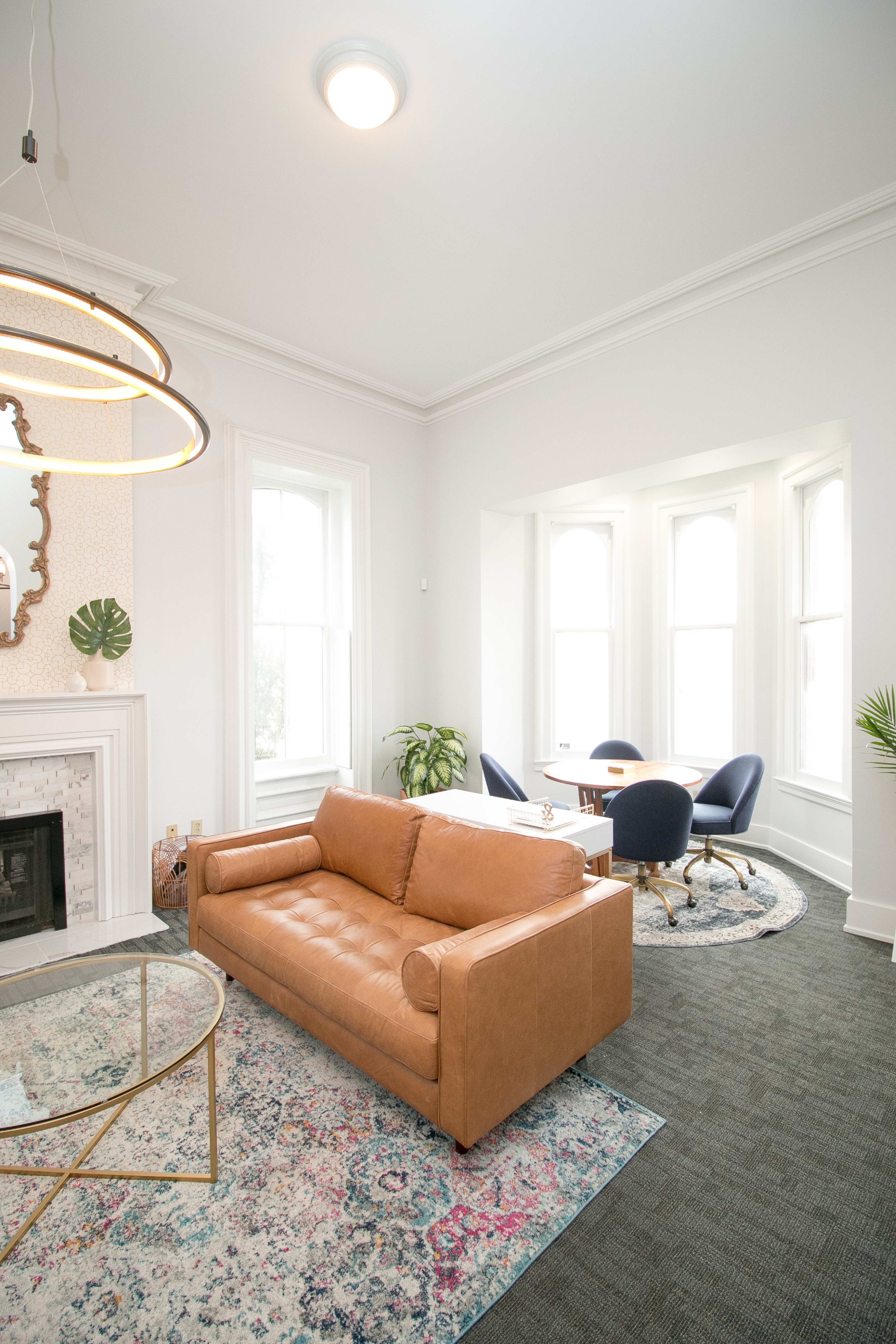A modern living area with a brown leather sofa, a round coffee table, and a corner with large windows.