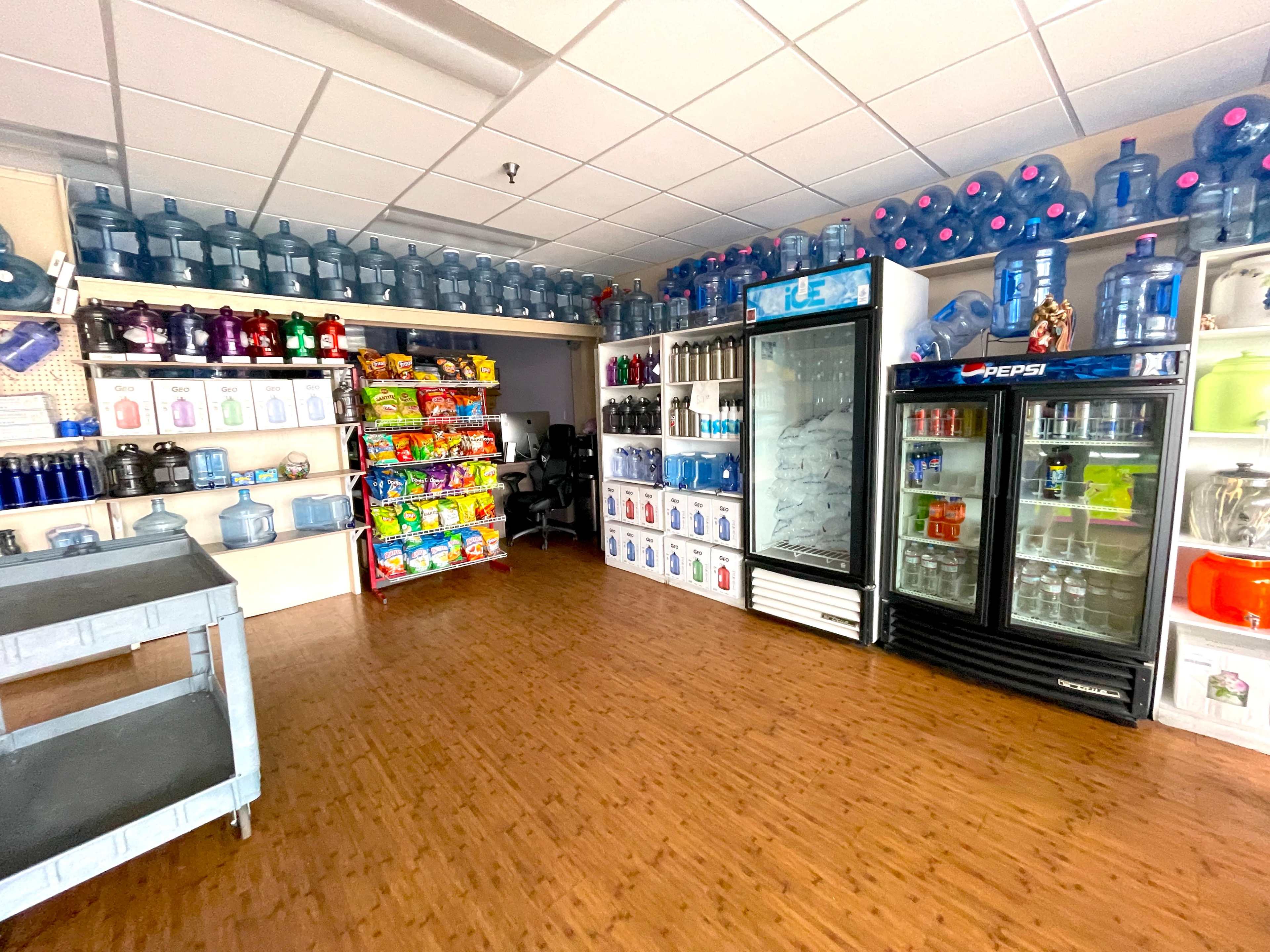 The image shows a shop interior filled with various beverage containers, including water bottles, soft drinks in a cooler, and shelves stocked with snacks.
