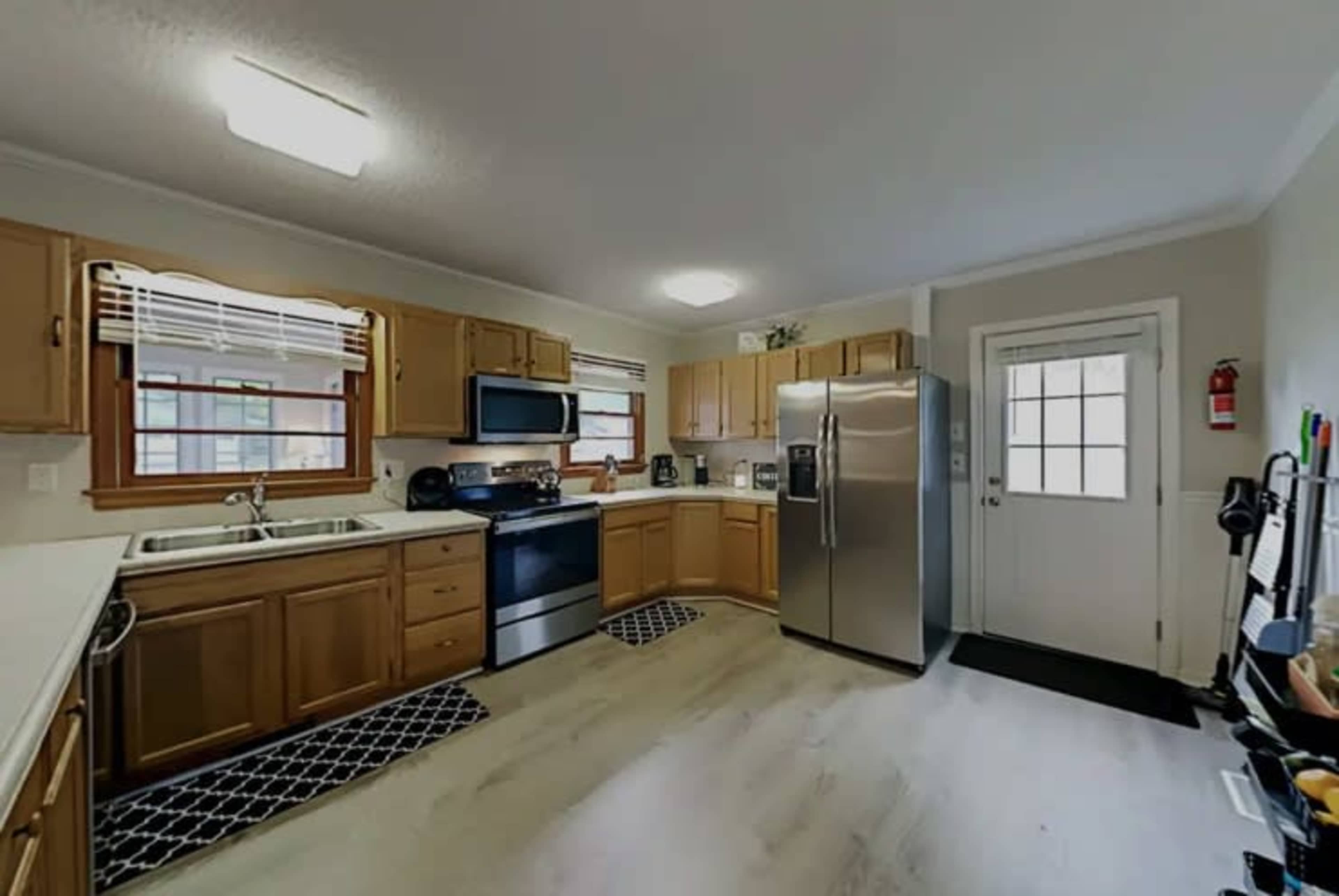 A kitchen features wooden cabinets, a stainless steel refrigerator, a black stove, and a white countertop with a window overlooking the outside.