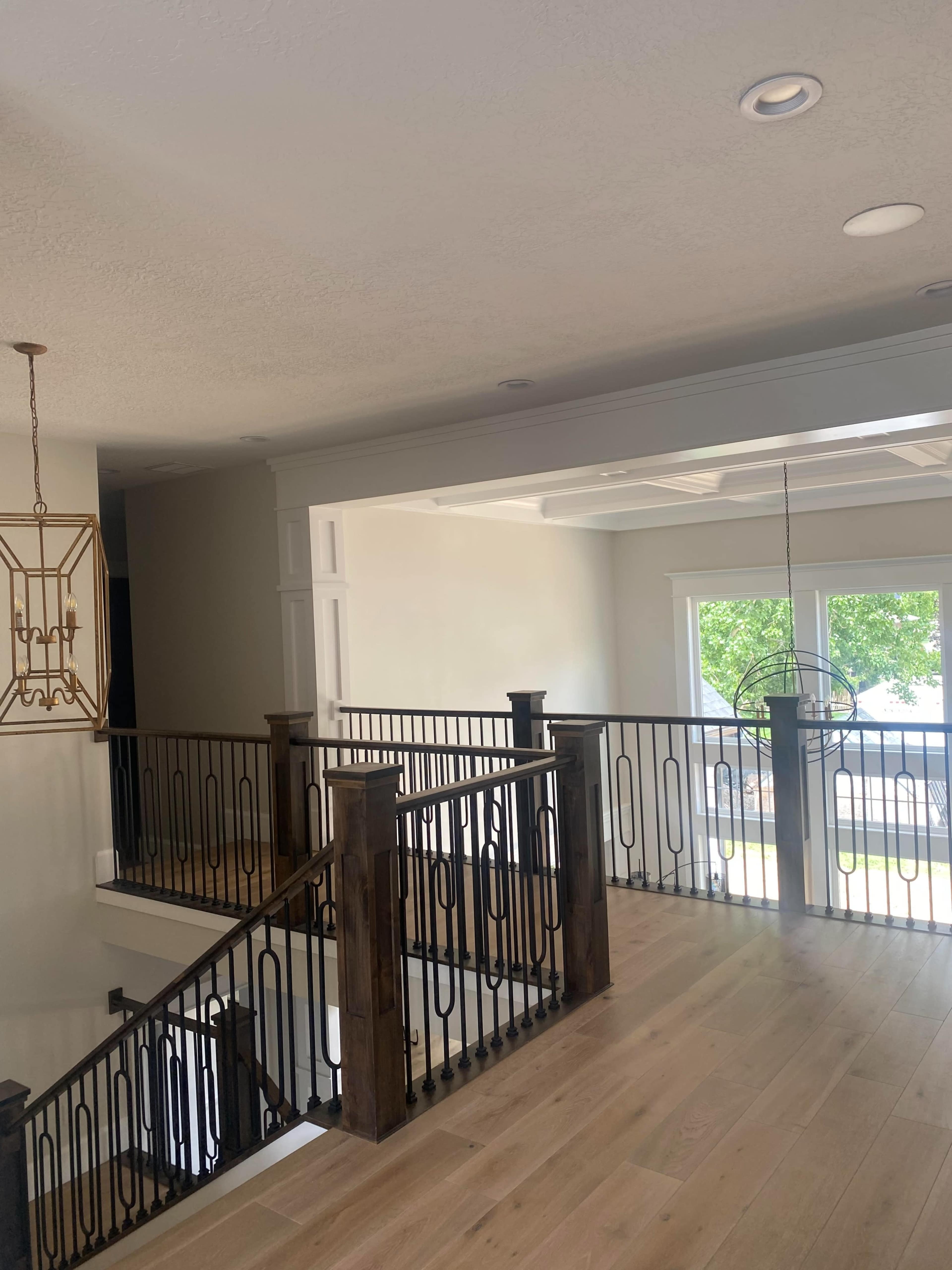 A modern interior space featuring a staircase with wooden railings and black decorative balusters, along with large windows that allow natural light to enter.