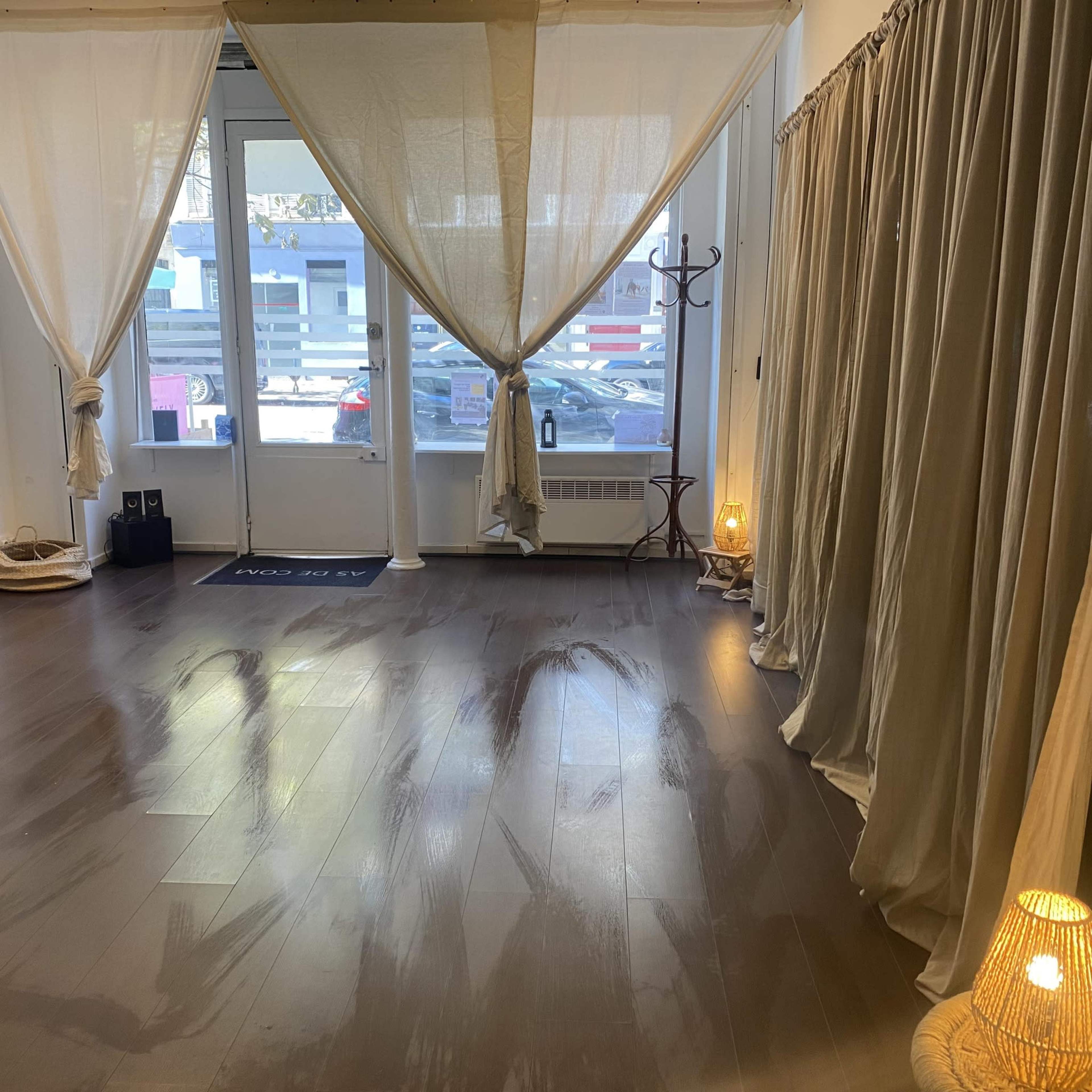 The image shows a spacious, well-lit room with light curtains draped at the entrance and wooden flooring.