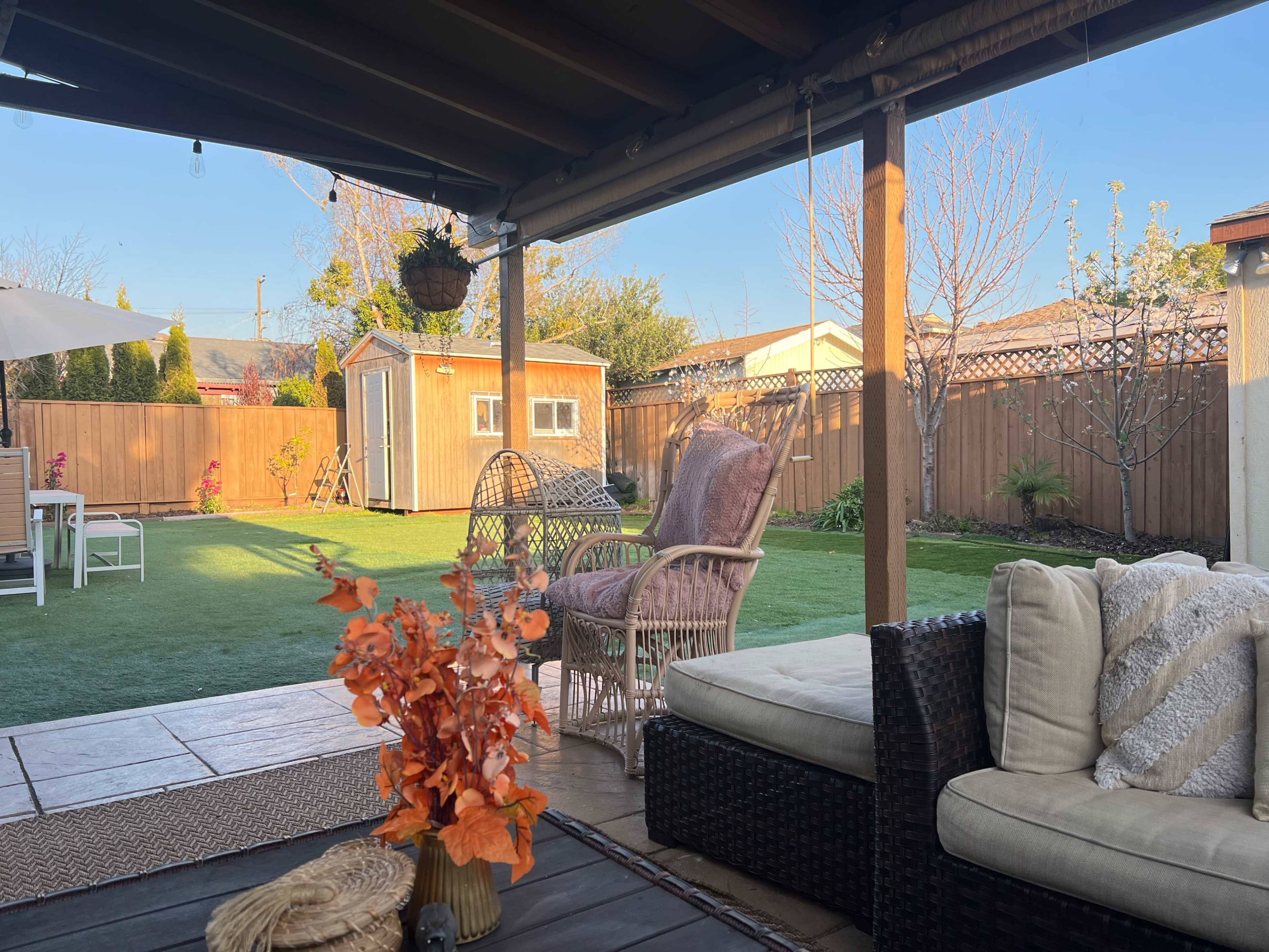 A backyard patio with seating arrangements, a small garden area, and a shed in the background.