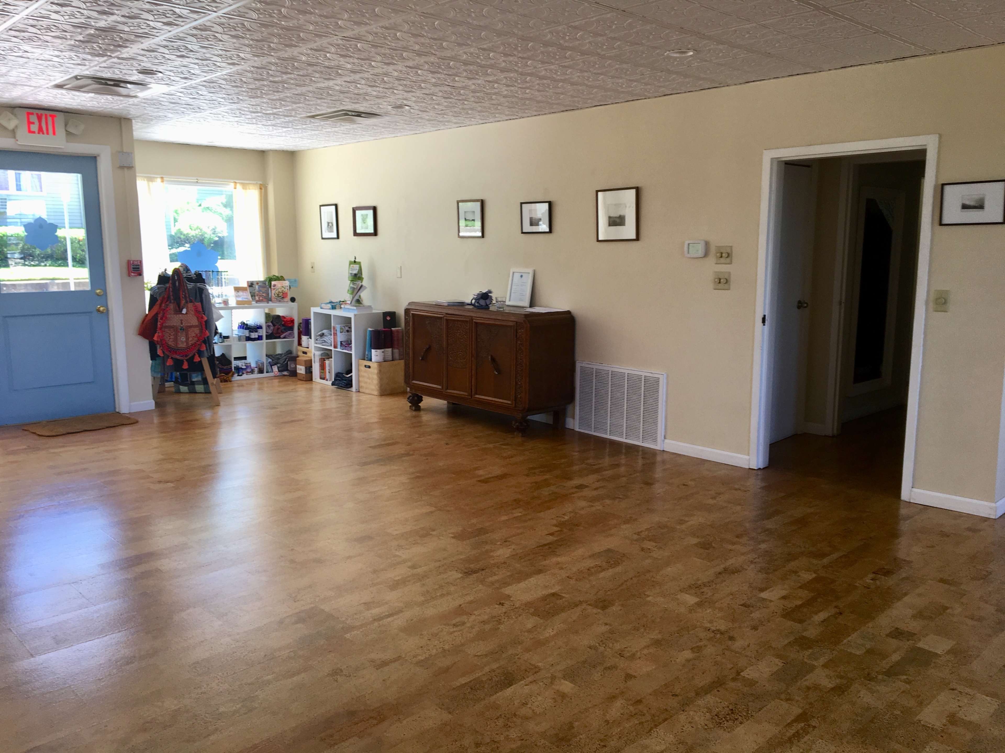 A spacious, empty room with light-colored walls, a wooden floor, and a blue door leading outside, along with a sideboard and shelves filled with items on one side.