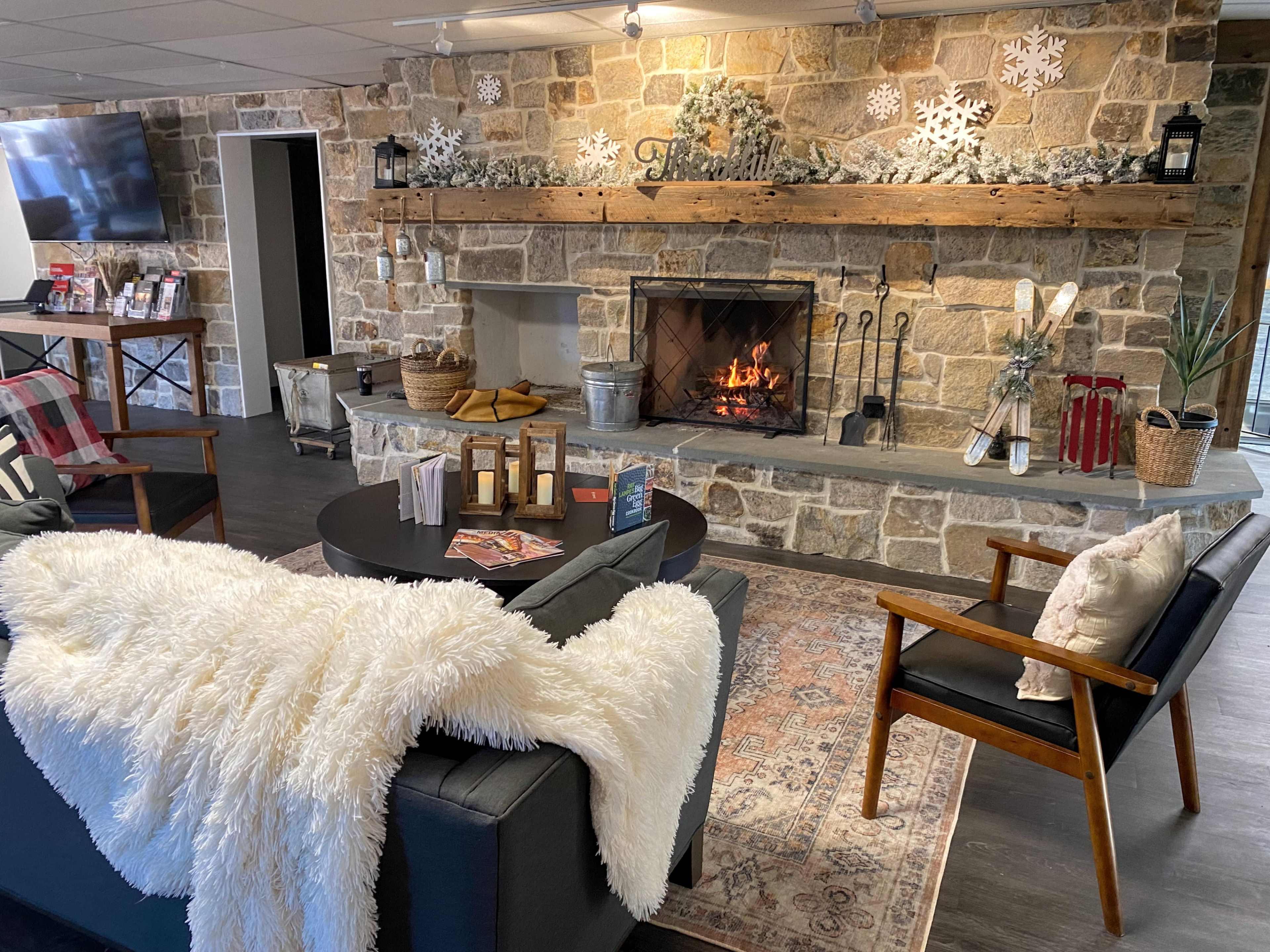 A cozy sitting area with a stone fireplace, wooden mantel, and a sofa draped with a white throw.