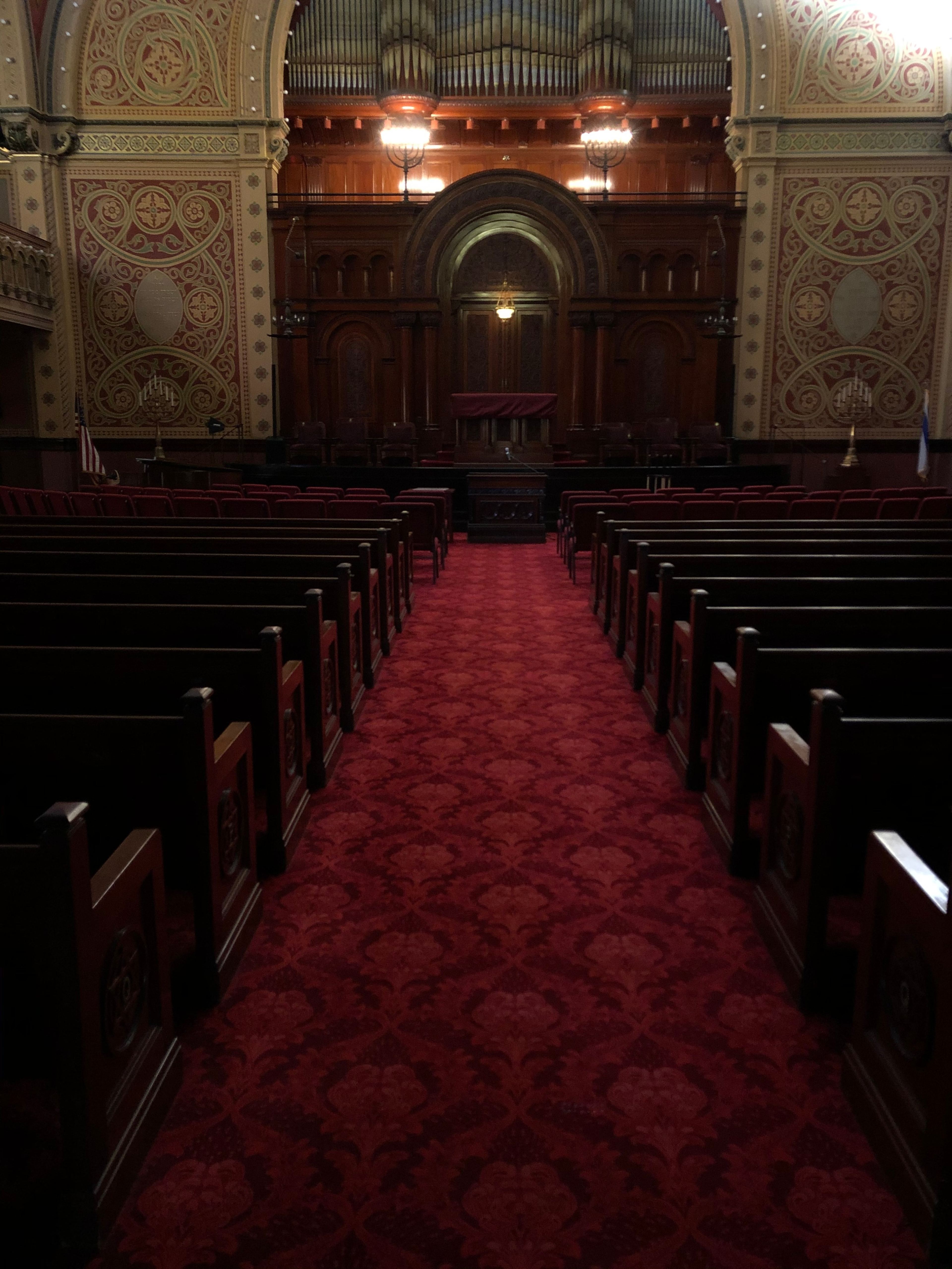 The interior of a historic assembly hall with wooden pews facing a raised podium beneath a decorative ceiling.