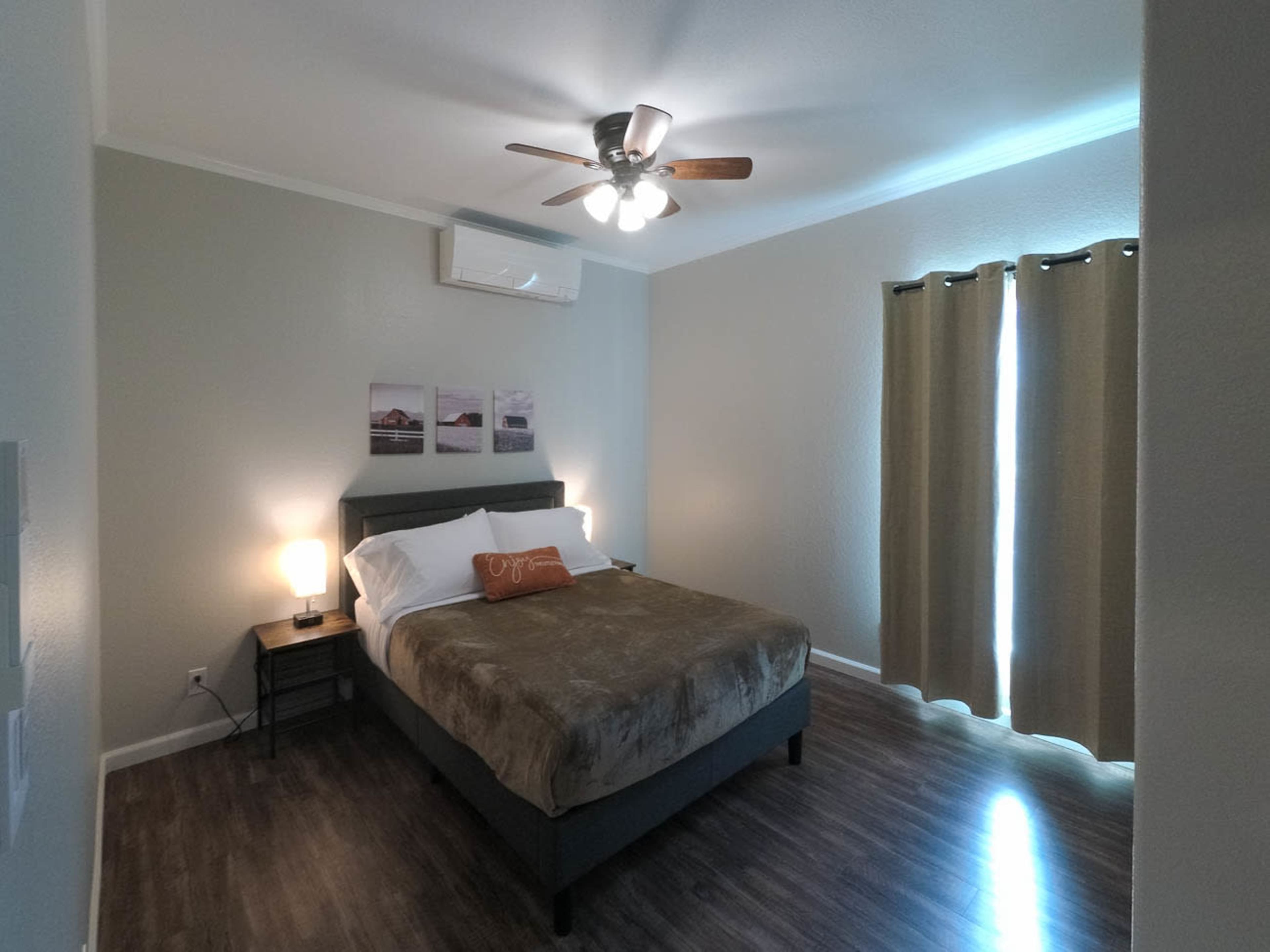 A bedroom featuring a bed with a comforter, a bedside lamp, a ceiling fan, and curtains over a window.