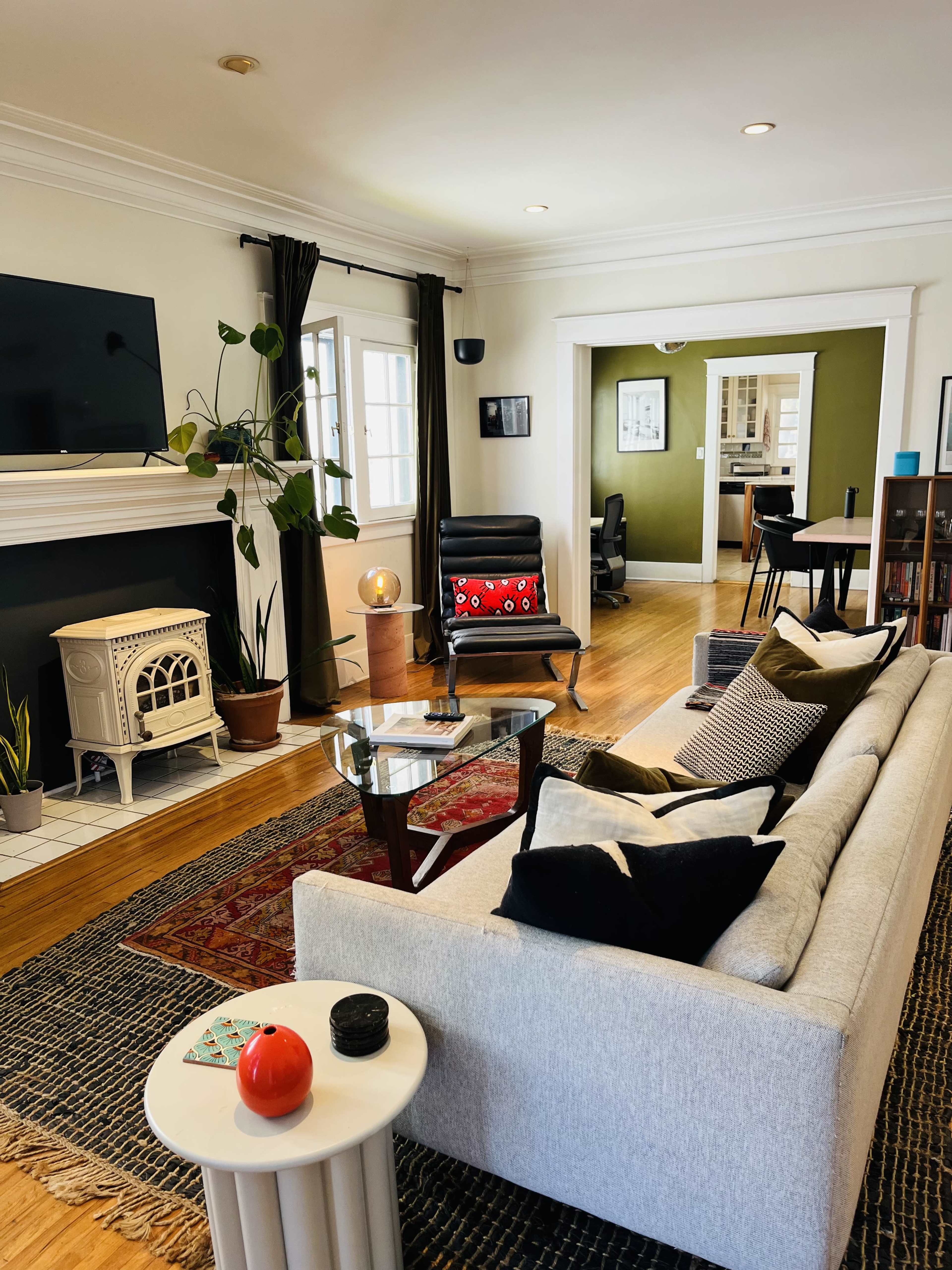 A modern living room featuring a light-colored sofa, a glass coffee table, a decorative rug, and a vintage-style fireplace surrounded by plants.