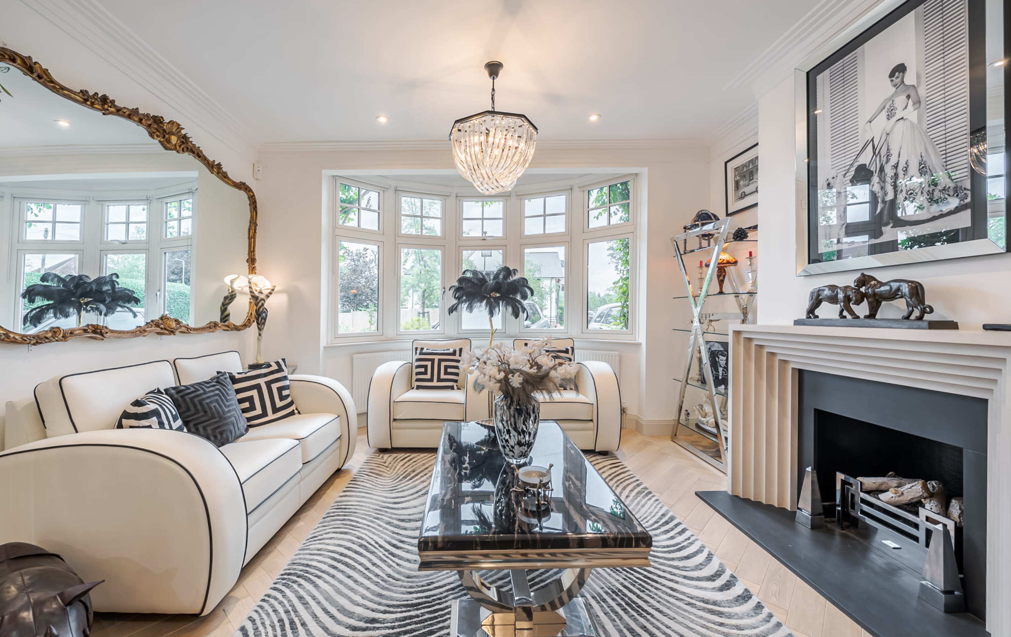 The living room features two white sofas, a glass coffee table, and a fireplace, with large windows allowing natural light to fill the space.