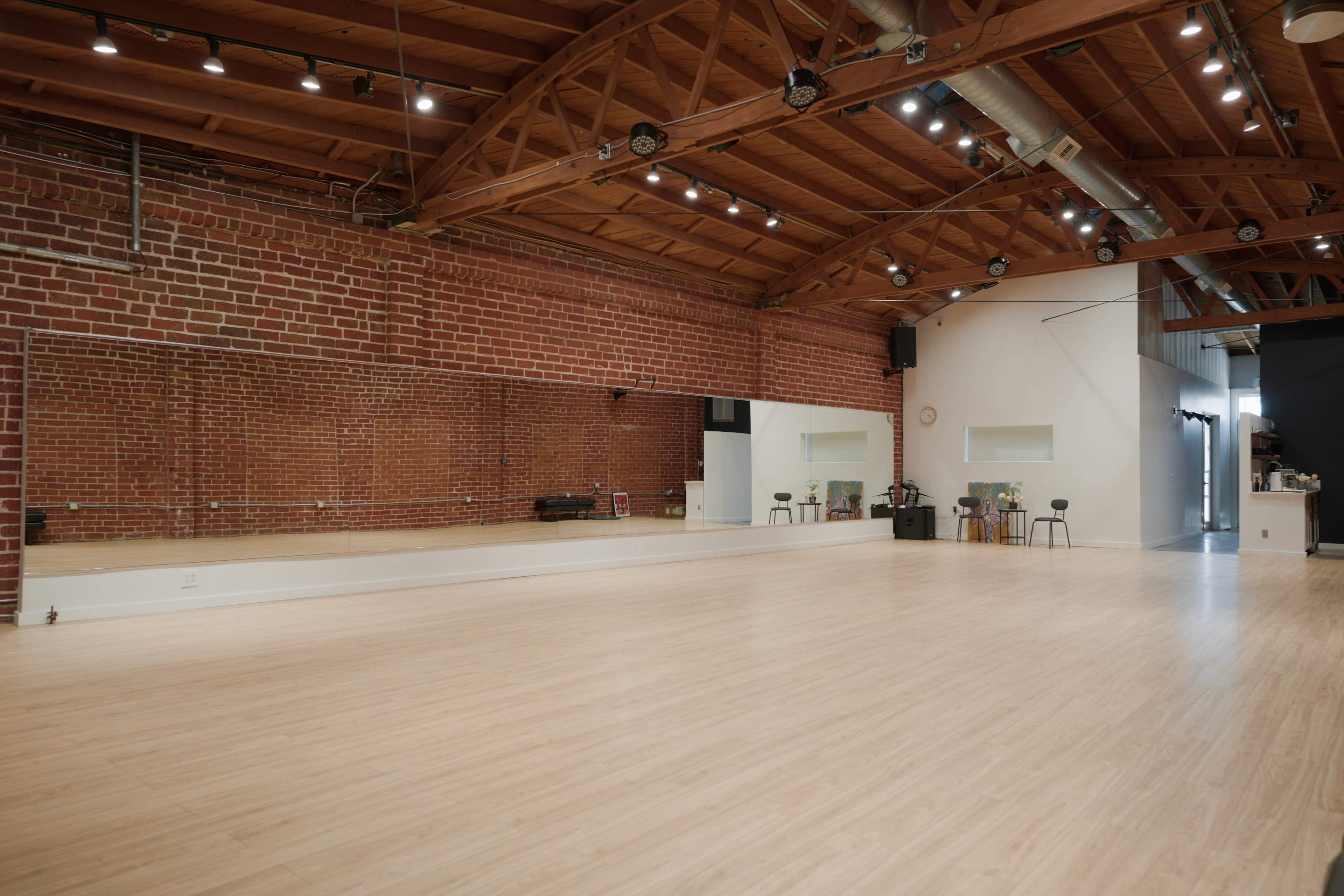 A spacious dance studio with wooden flooring, exposed brick walls, and a large mirror along one side.