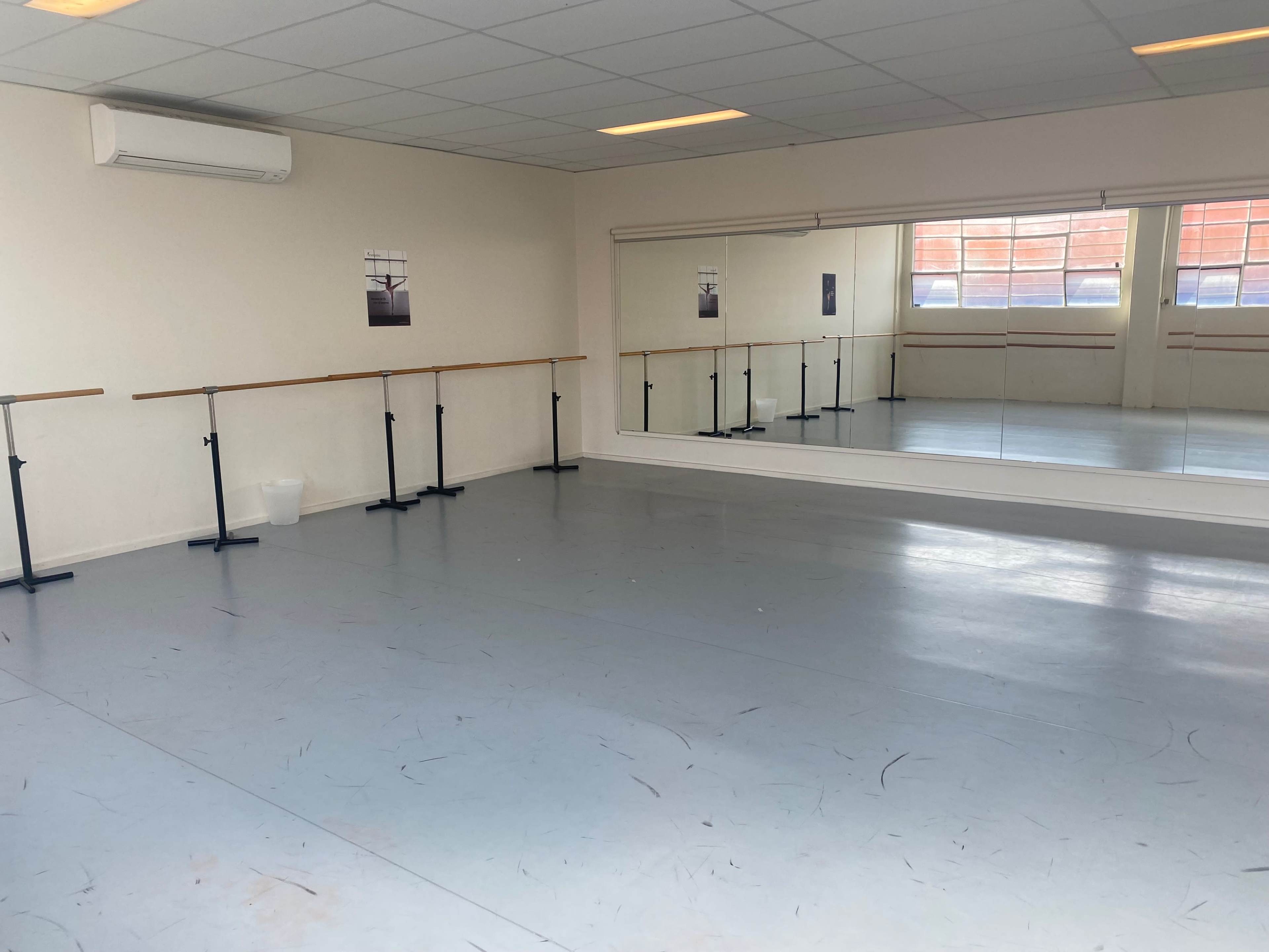 A dance studio with a mirrored wall, ballet barres, and a clean, light-colored floor.