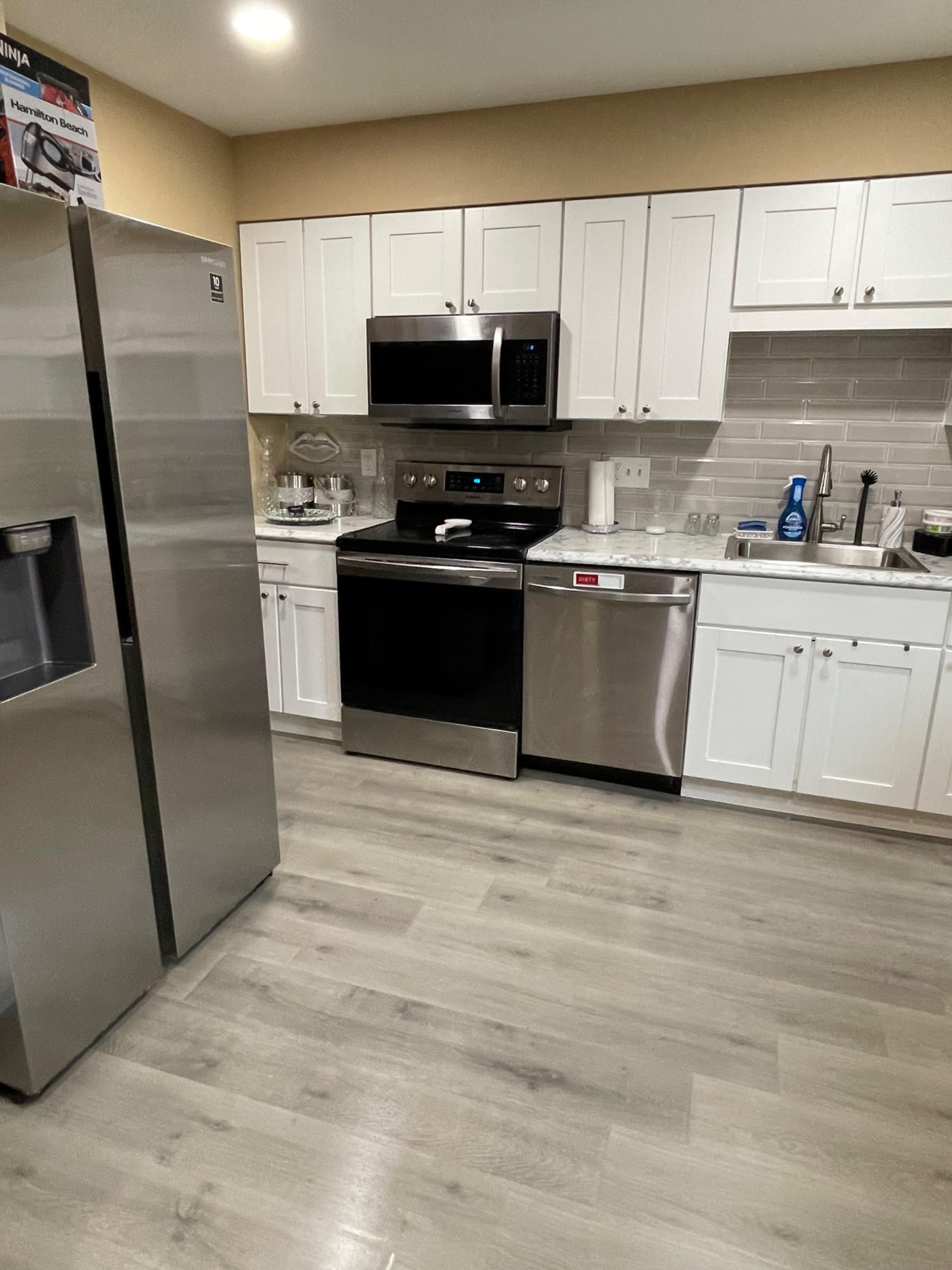 A modern kitchen featuring stainless steel appliances, white cabinets, and a gray tiled backsplash.