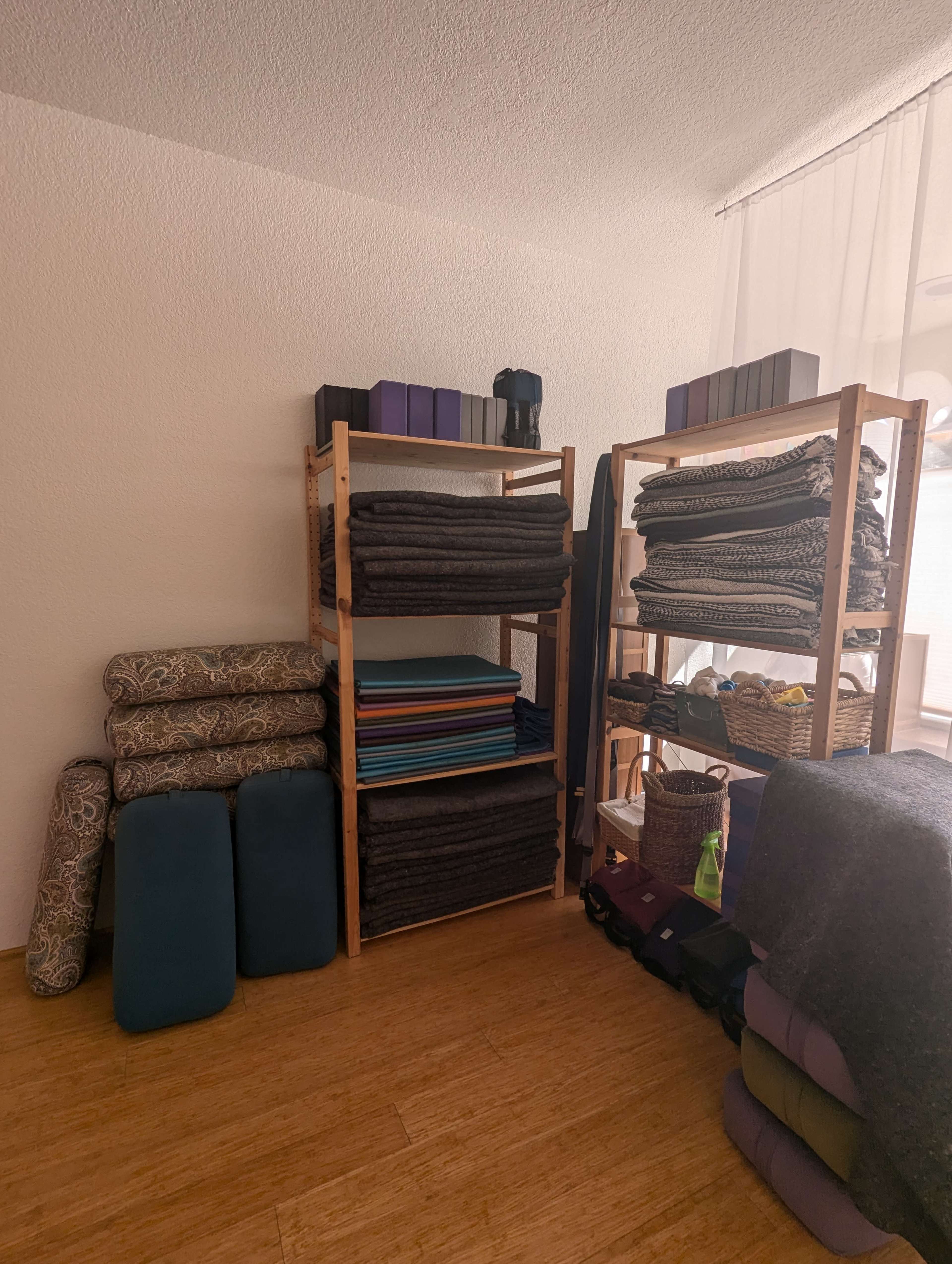 A room with wooden shelves stacked with neatly arranged yoga mats, blankets, and props.