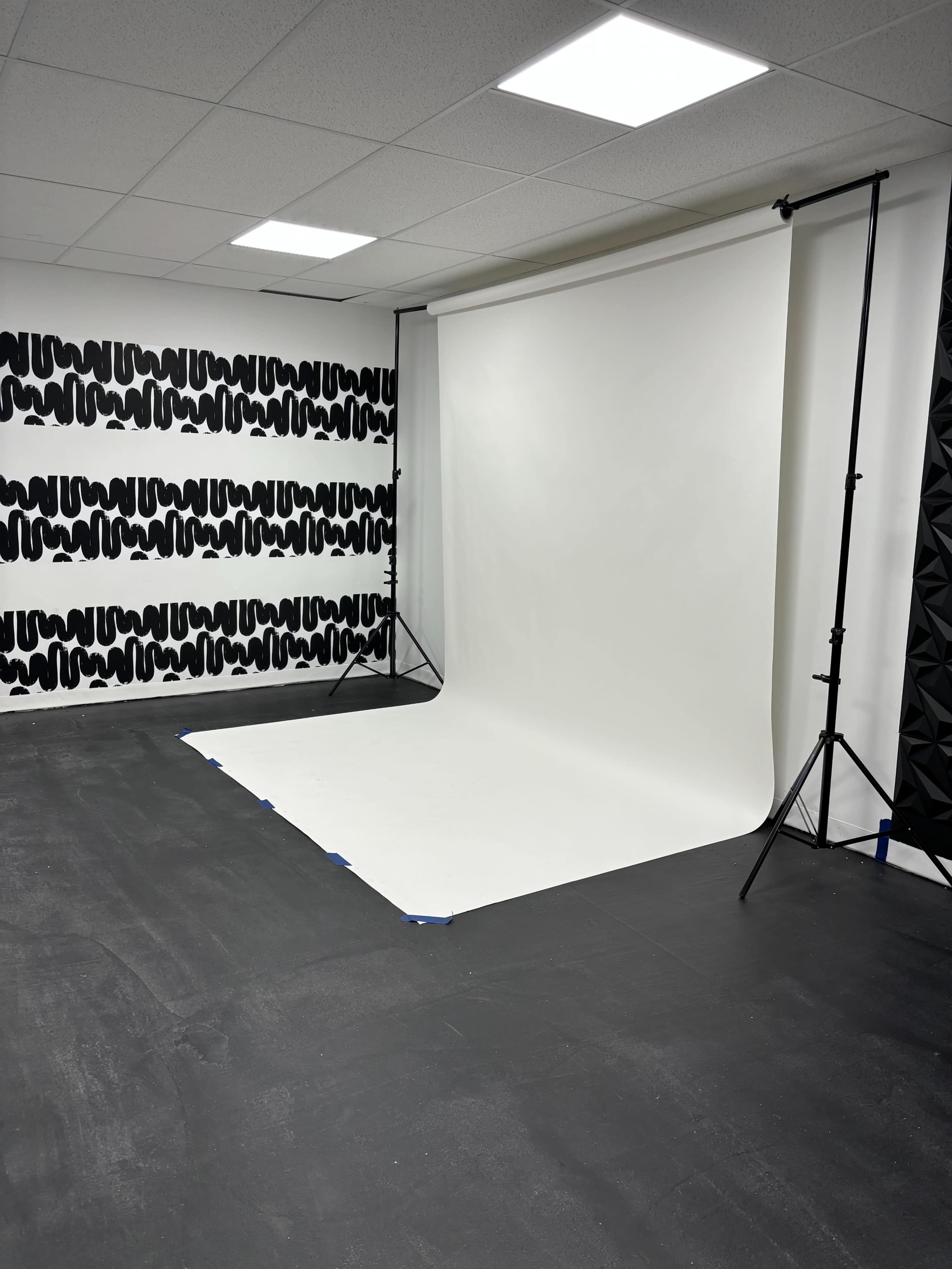 The image shows a photography studio featuring a white backdrop set up on the floor and a patterned wall on one side.