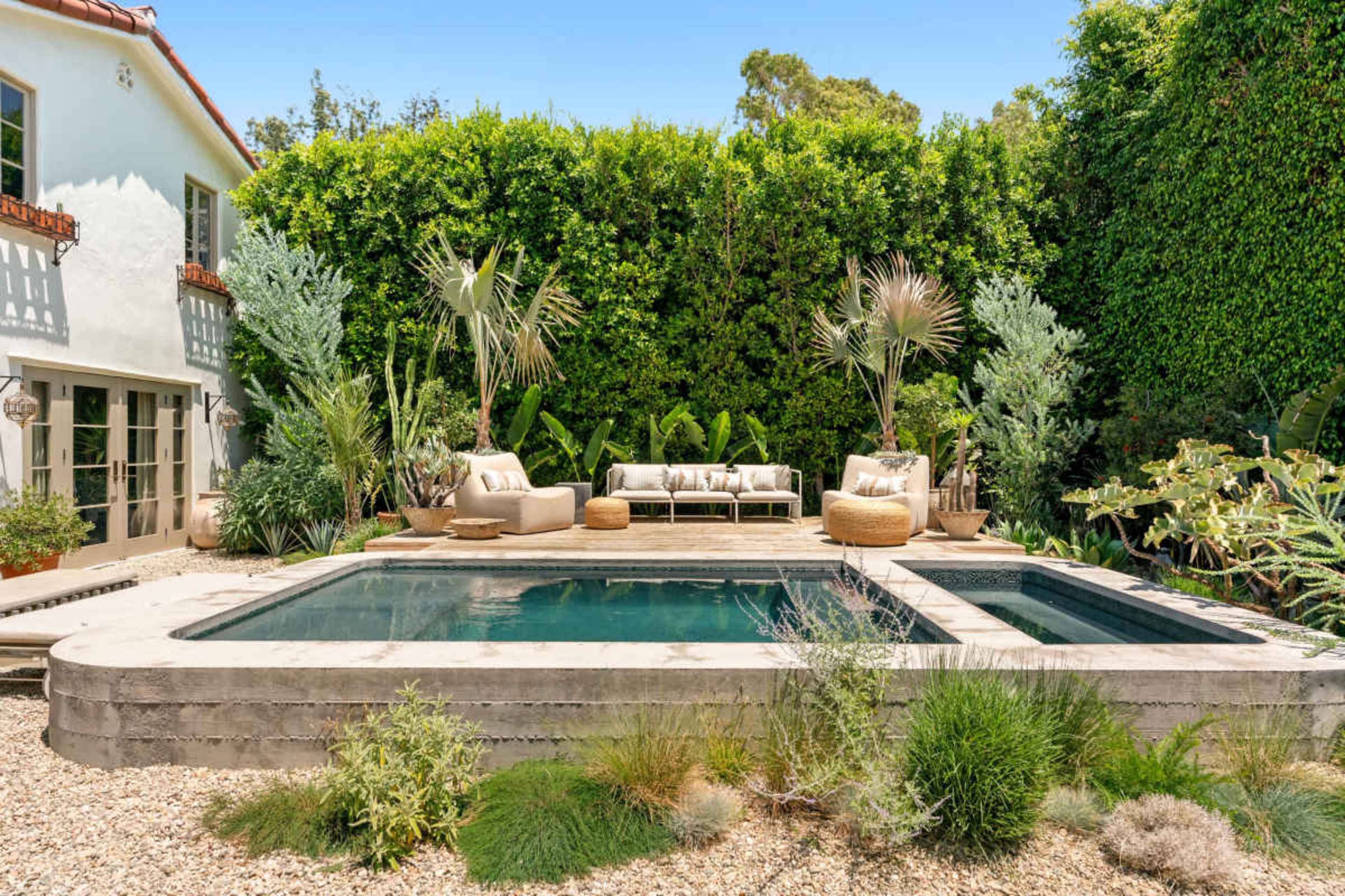 The image shows a backyard oasis featuring a rectangular swimming pool surrounded by plants, seating, and decorative stones.