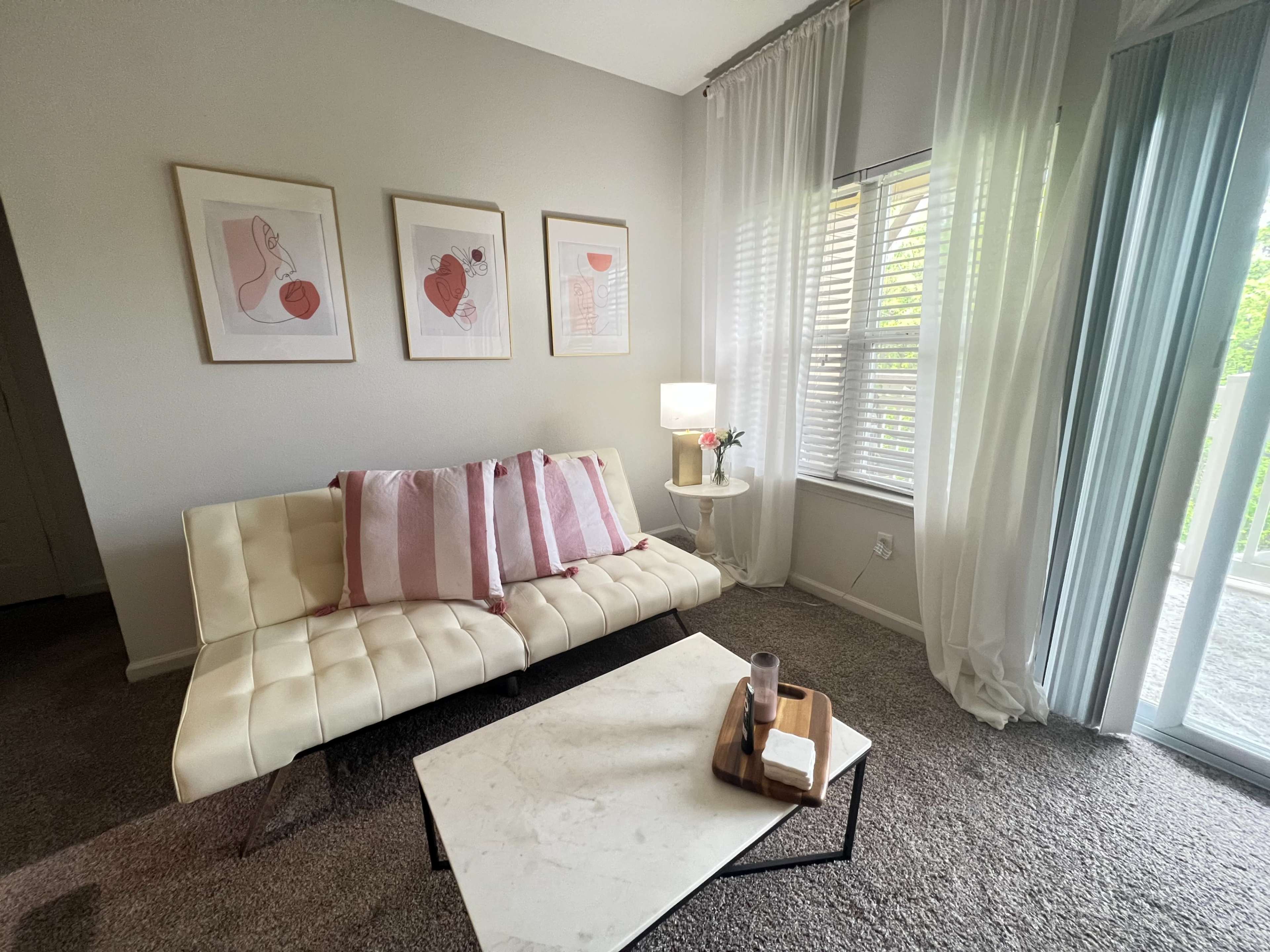 A light-colored living room featuring a white sofa with pink striped pillows, a marble coffee table, and framed artwork on the wall.