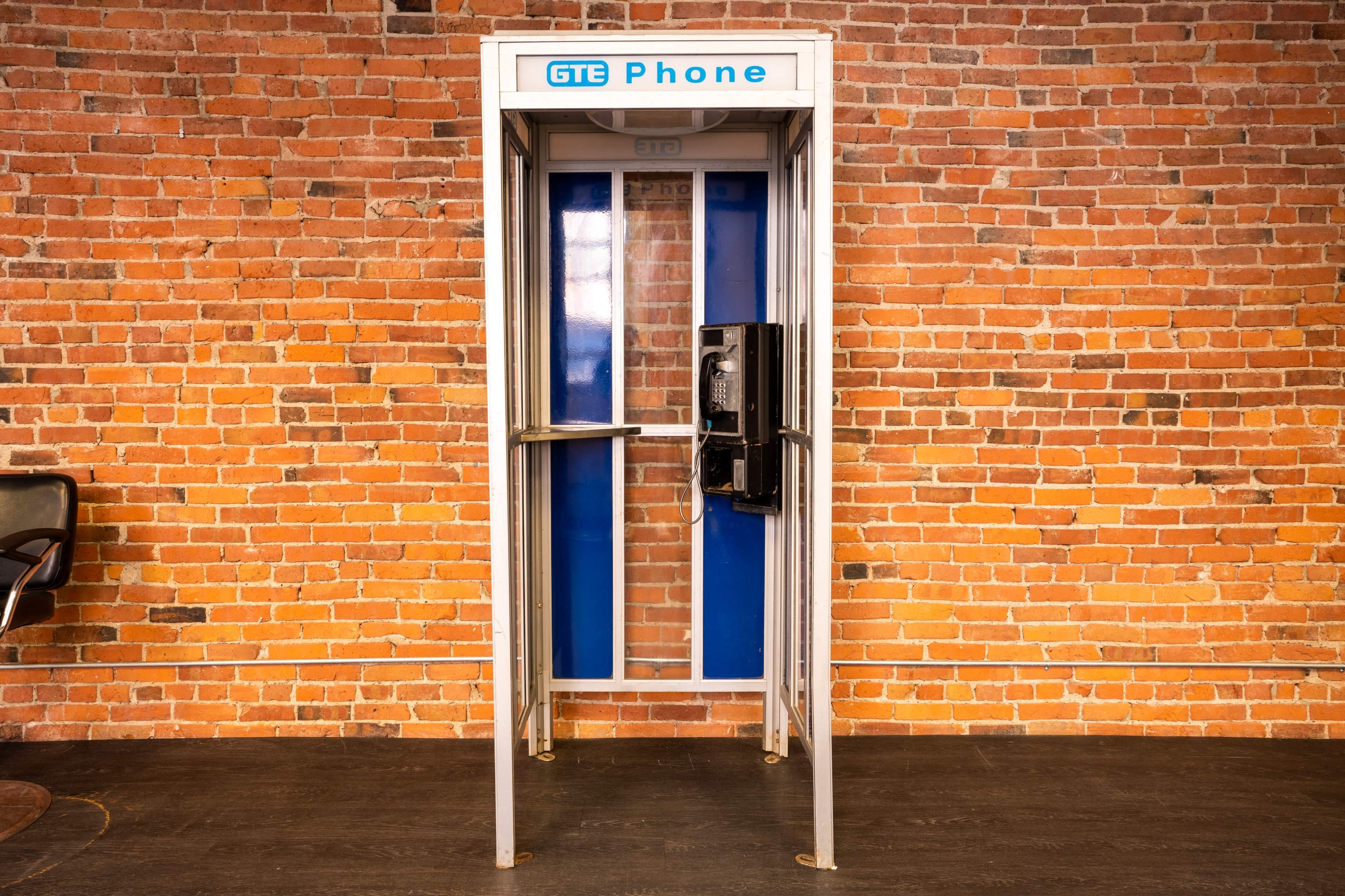 A GTE phone booth standing against a brick wall.