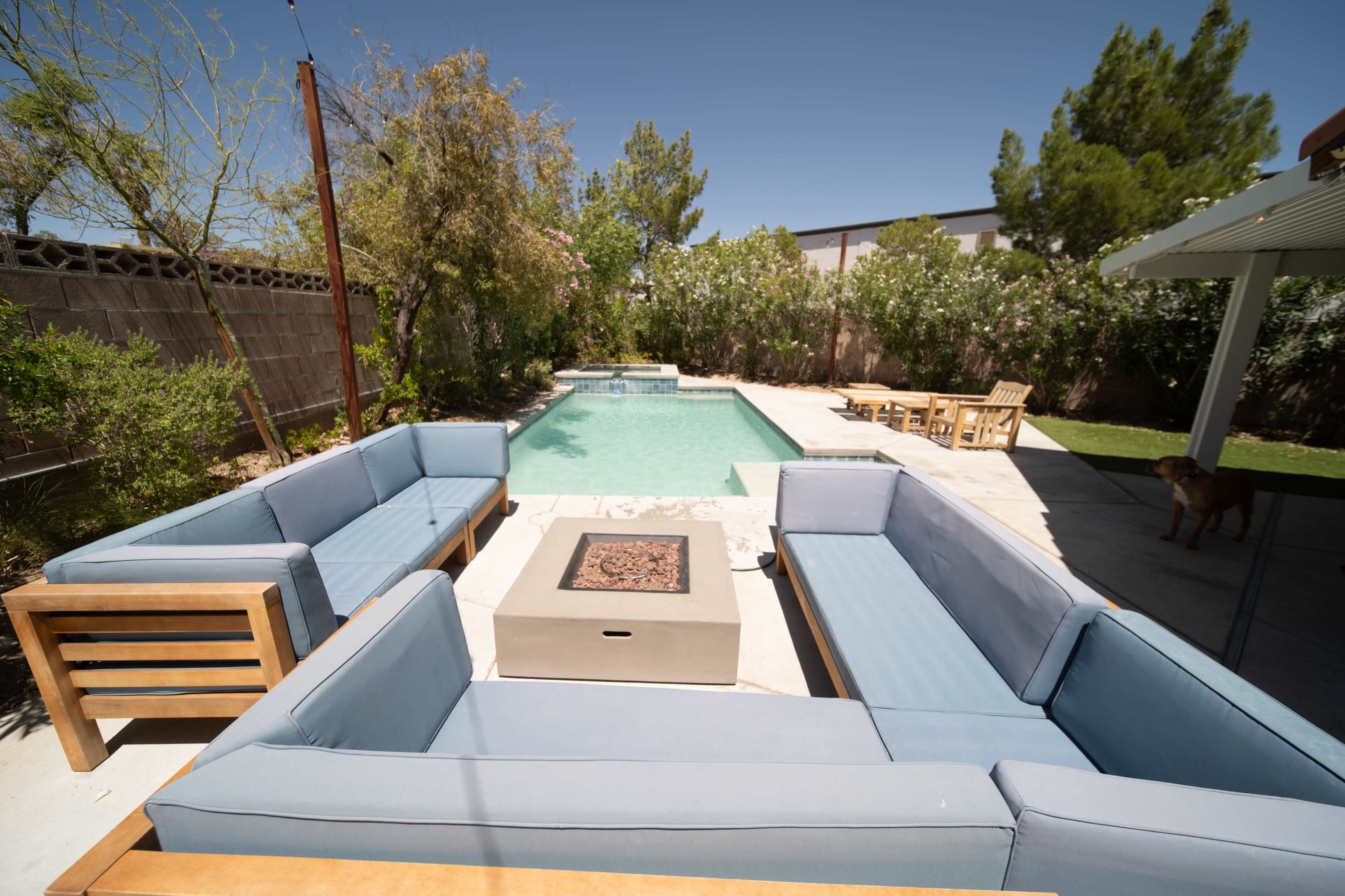 A spacious outdoor seating area surrounds a rectangular swimming pool, featuring wooden furniture and a coffee table in the center.