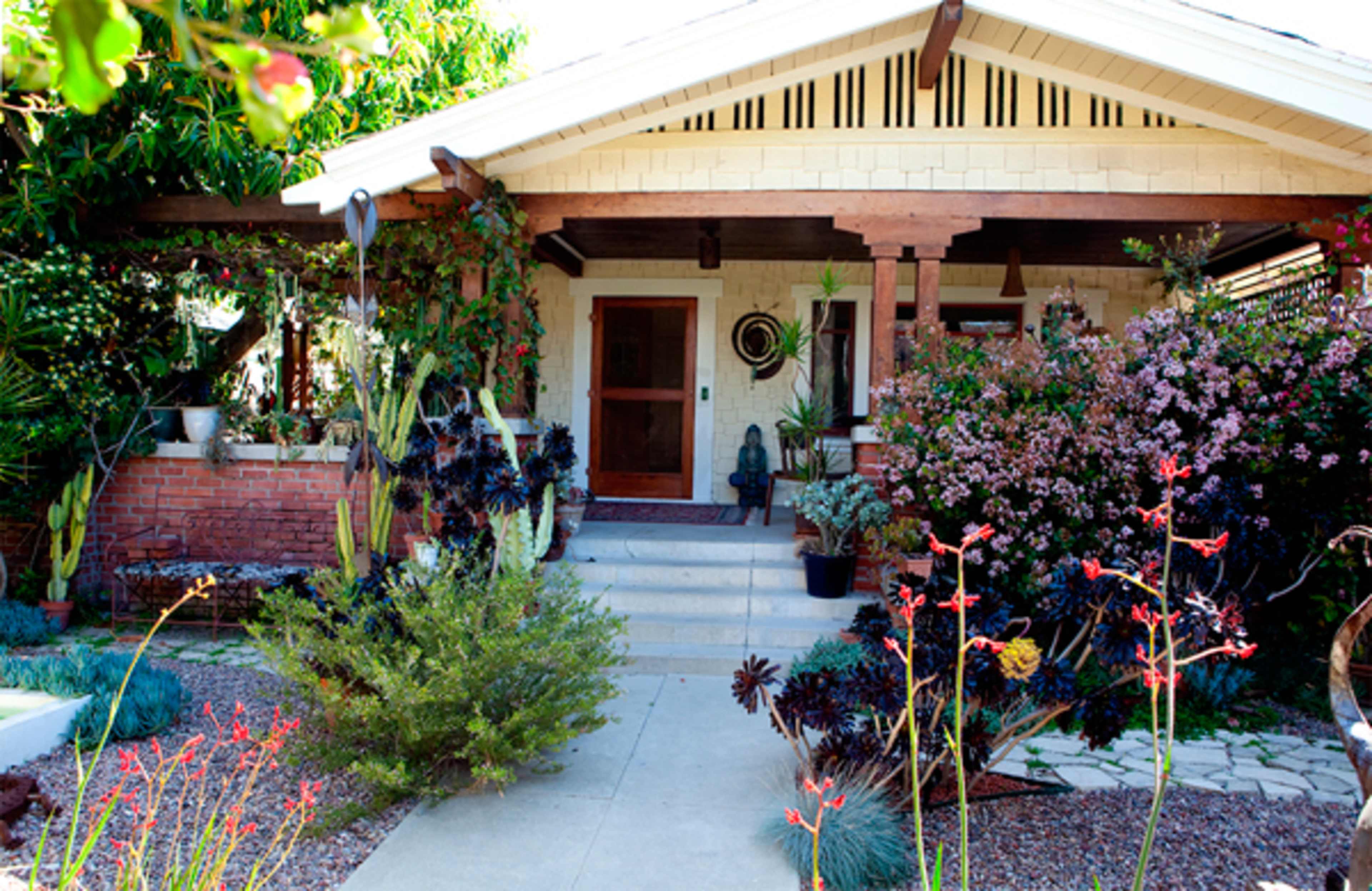 A front porch features a wooden structure with plants and flowers surrounding the entrance to a house.