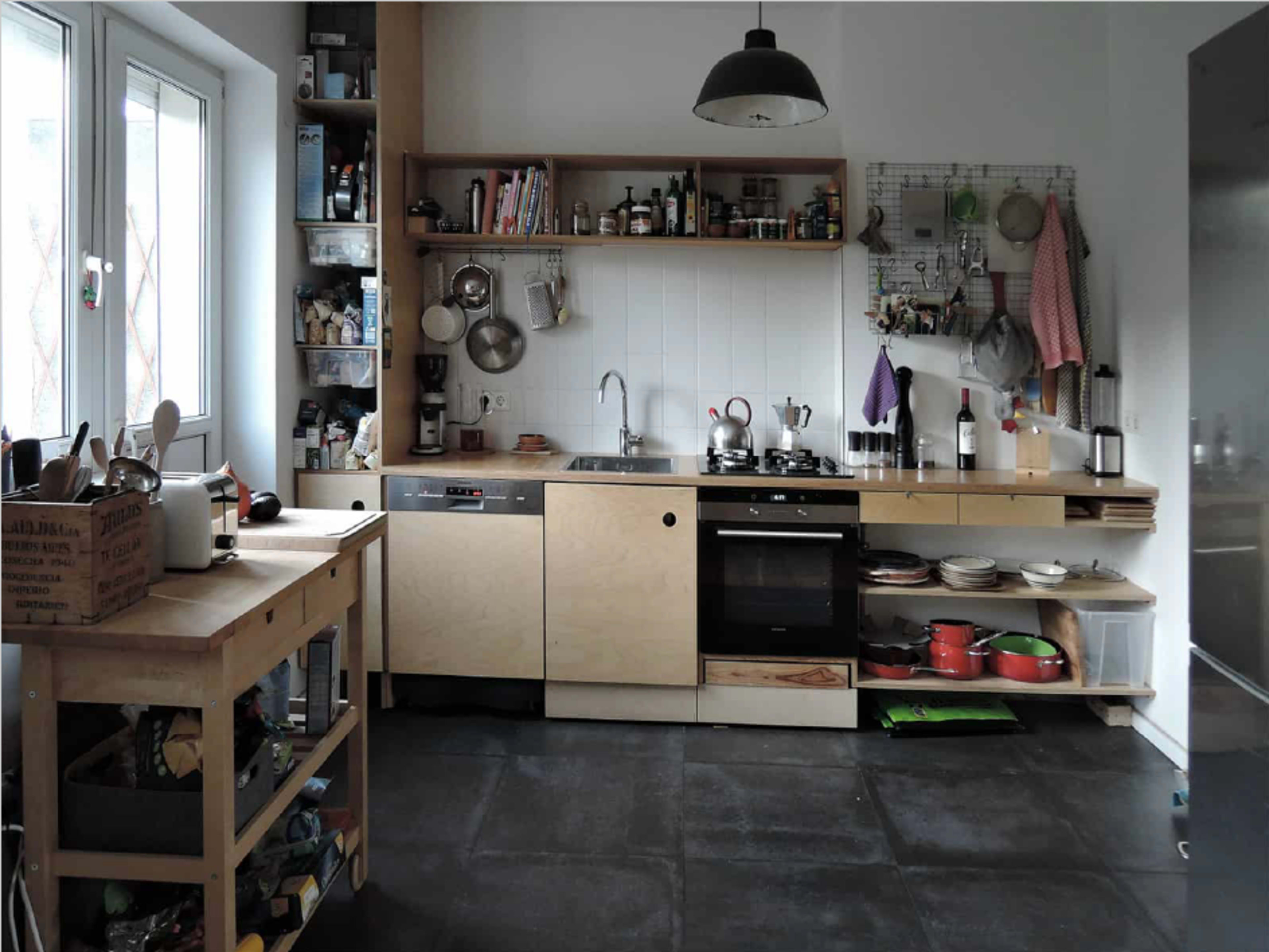 A modern kitchen features wooden cabinets, a stainless steel stove, various cooking utensils, and a countertop with shelves displaying jars and dishware.