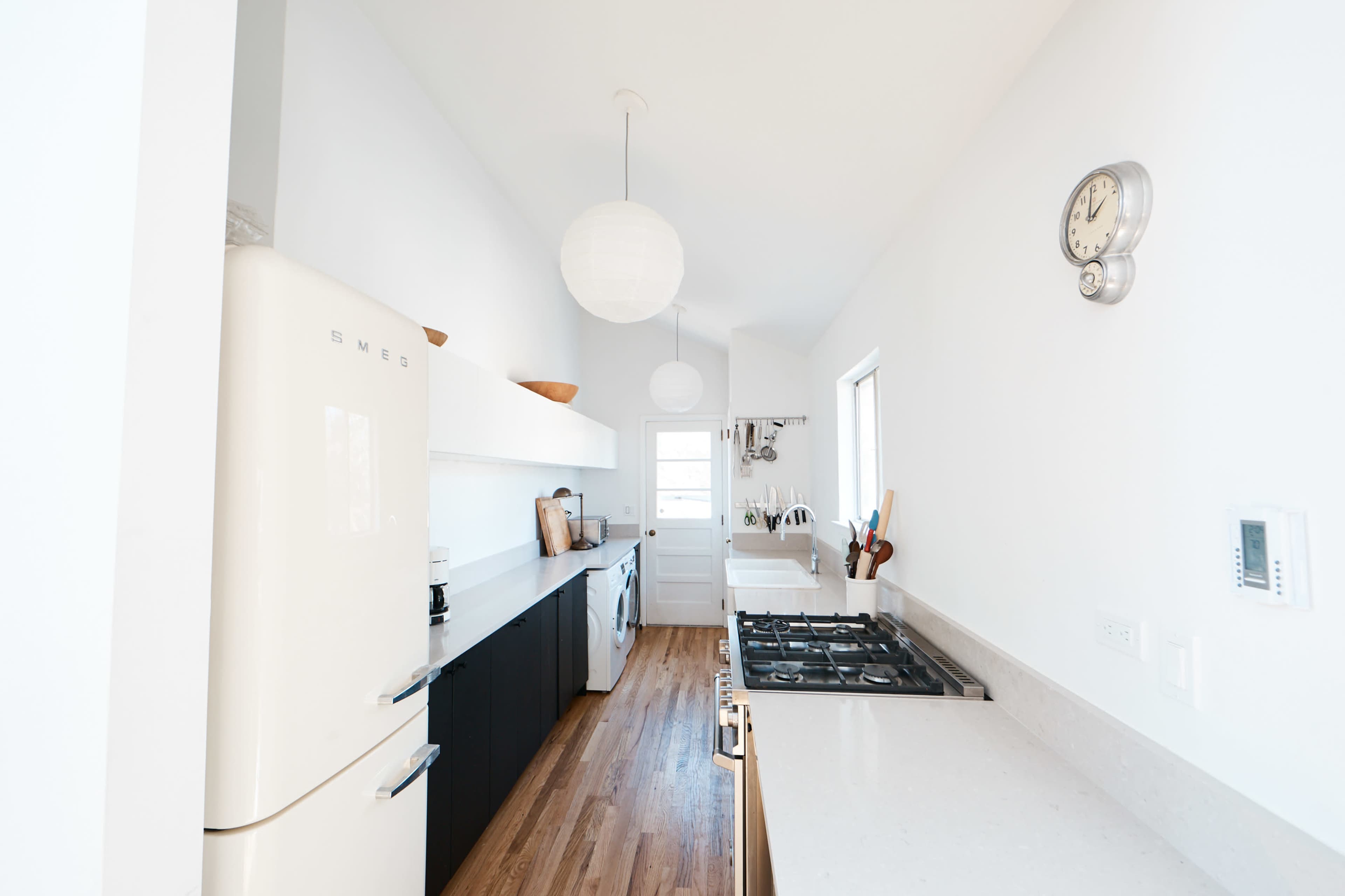 A modern kitchen with a white color scheme, featuring a vintage-style refrigerator, a gas stove, and wooden flooring.