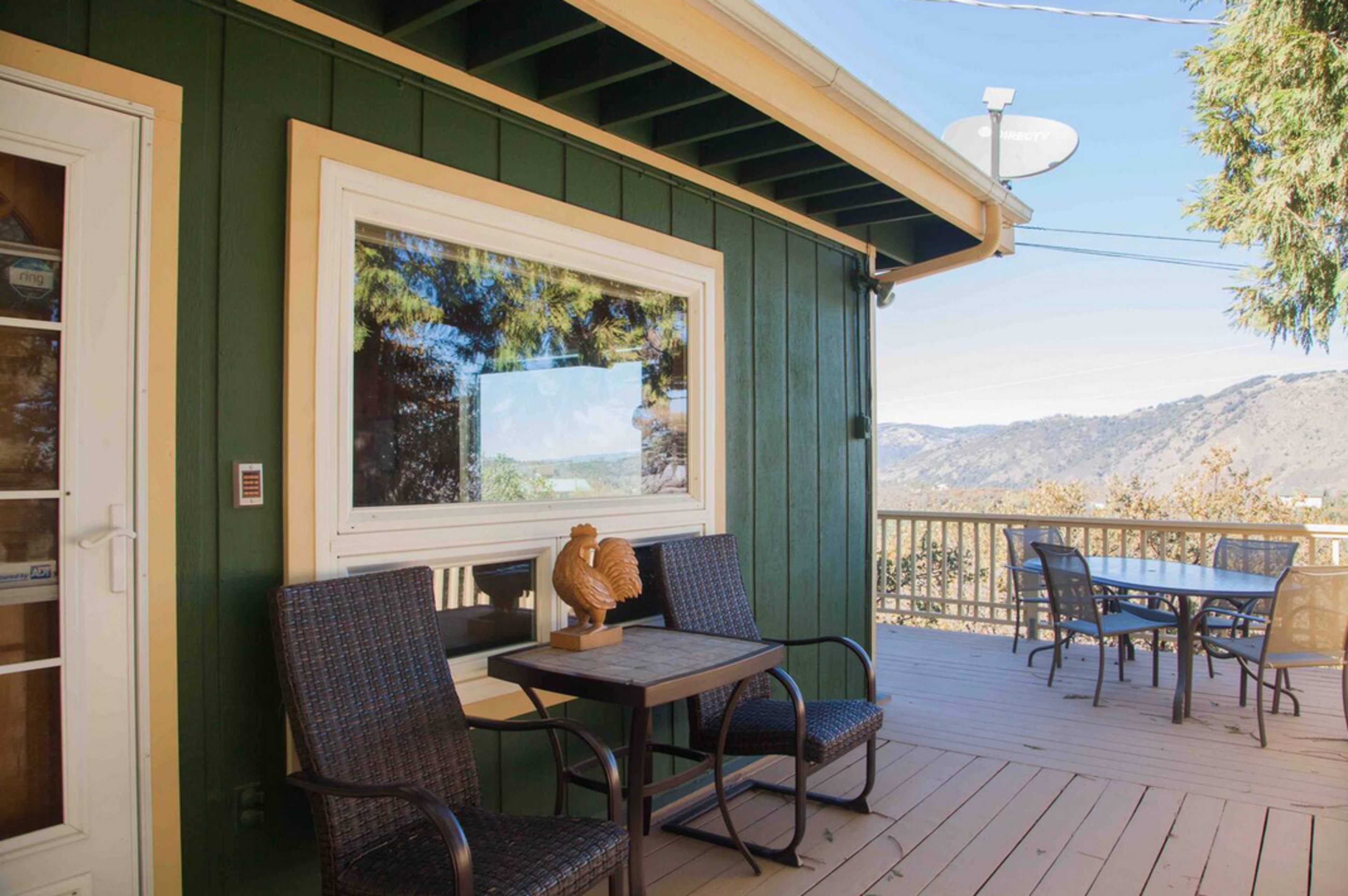 A porch with two chairs and a small table overlooks a scenic view of mountains and trees.