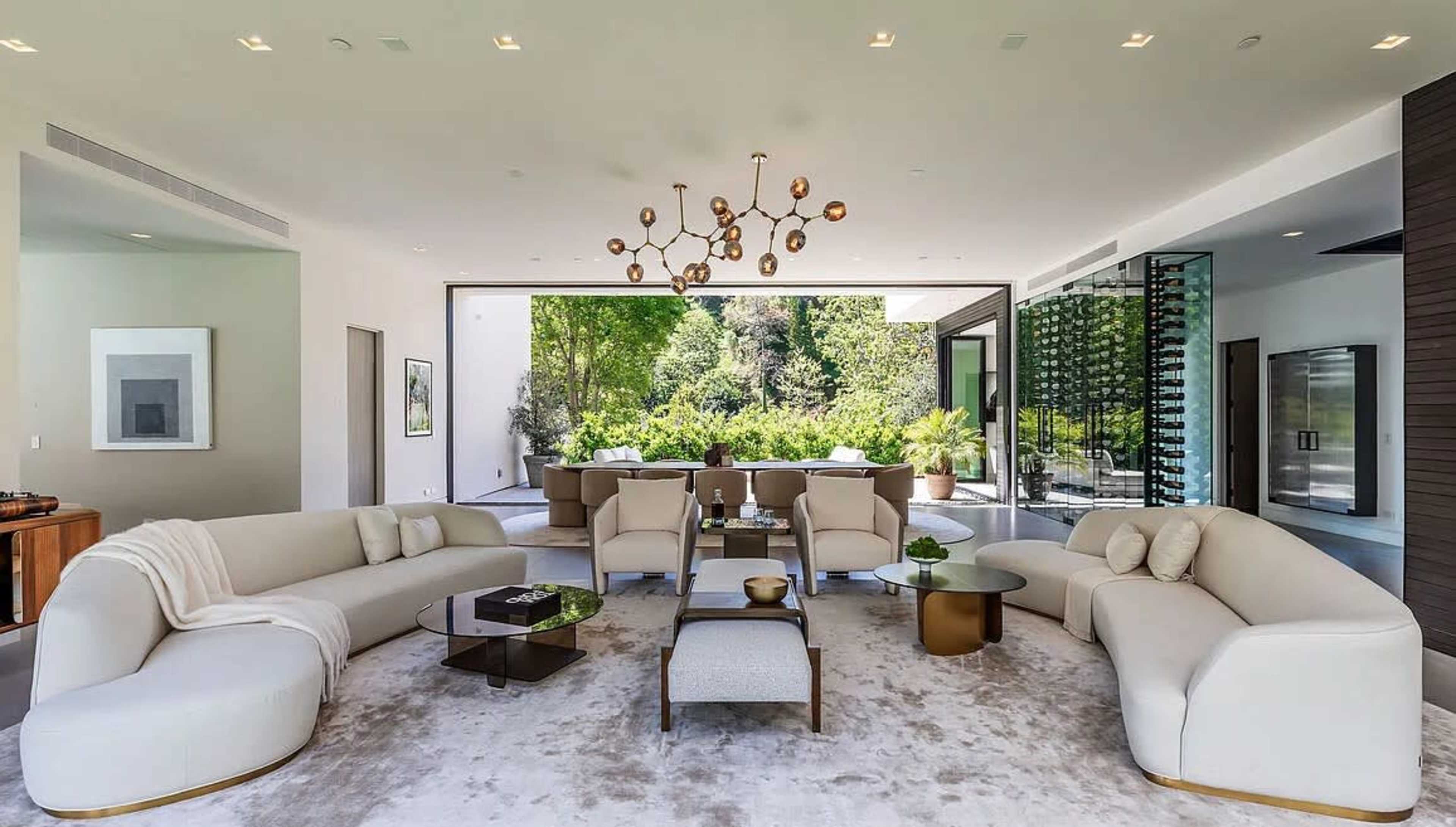 The image shows a modern living room with two curved sofas, a round coffee table, and large glass doors opening to a garden.