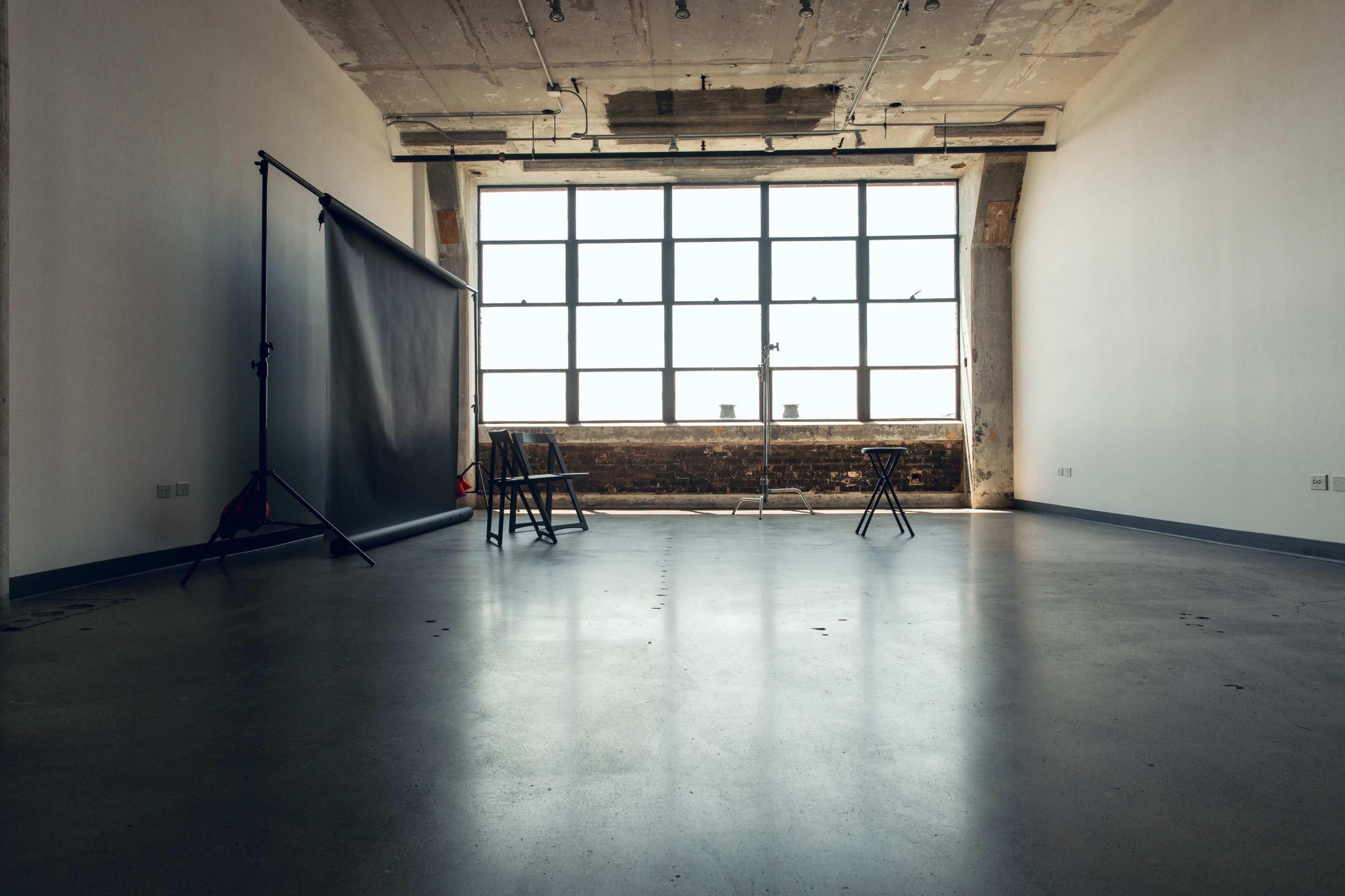 An empty room with a large window and a backdrop setup for photography.