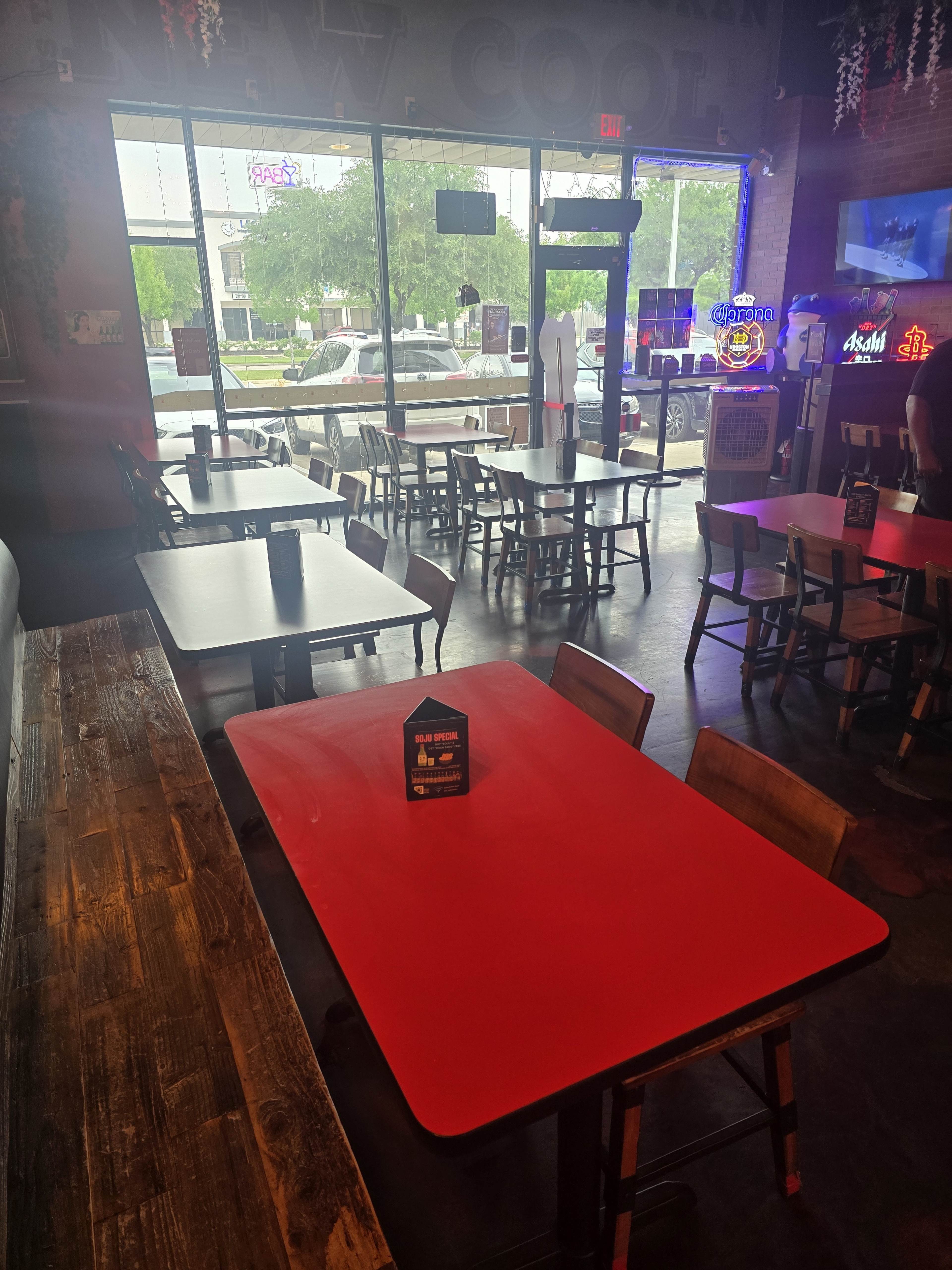 The image shows a restaurant interior with several tables, including a red table in the foreground, and a large window that provides a view of the outside.