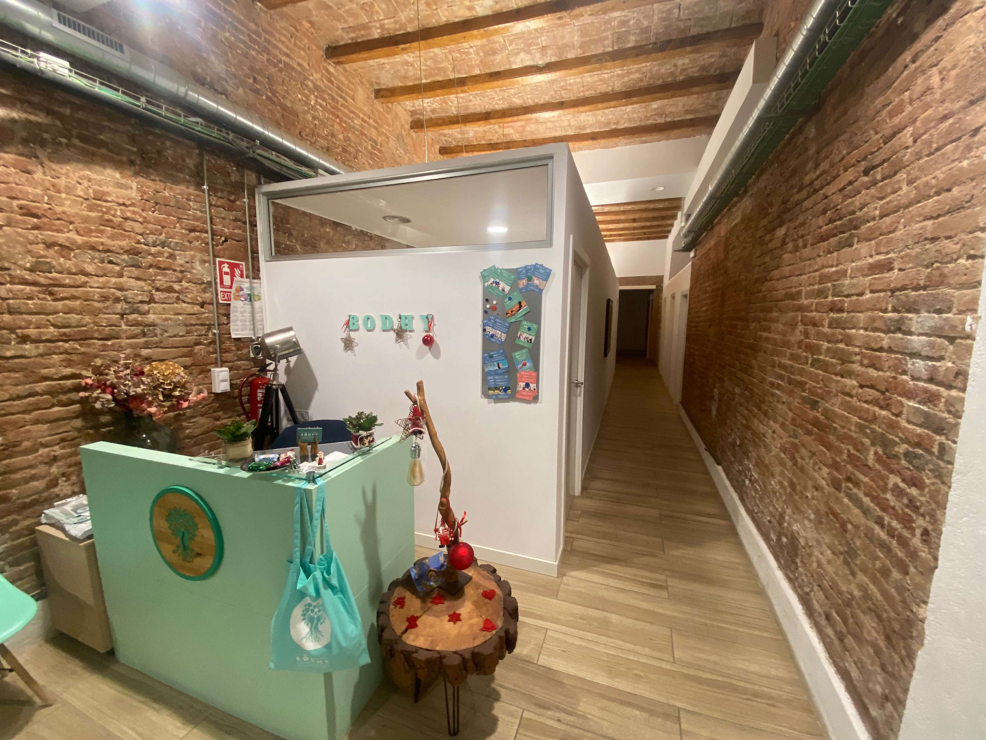 The image shows a narrow hallway with exposed brick walls, featuring a reception area with a wooden table and decorative elements on the left side.