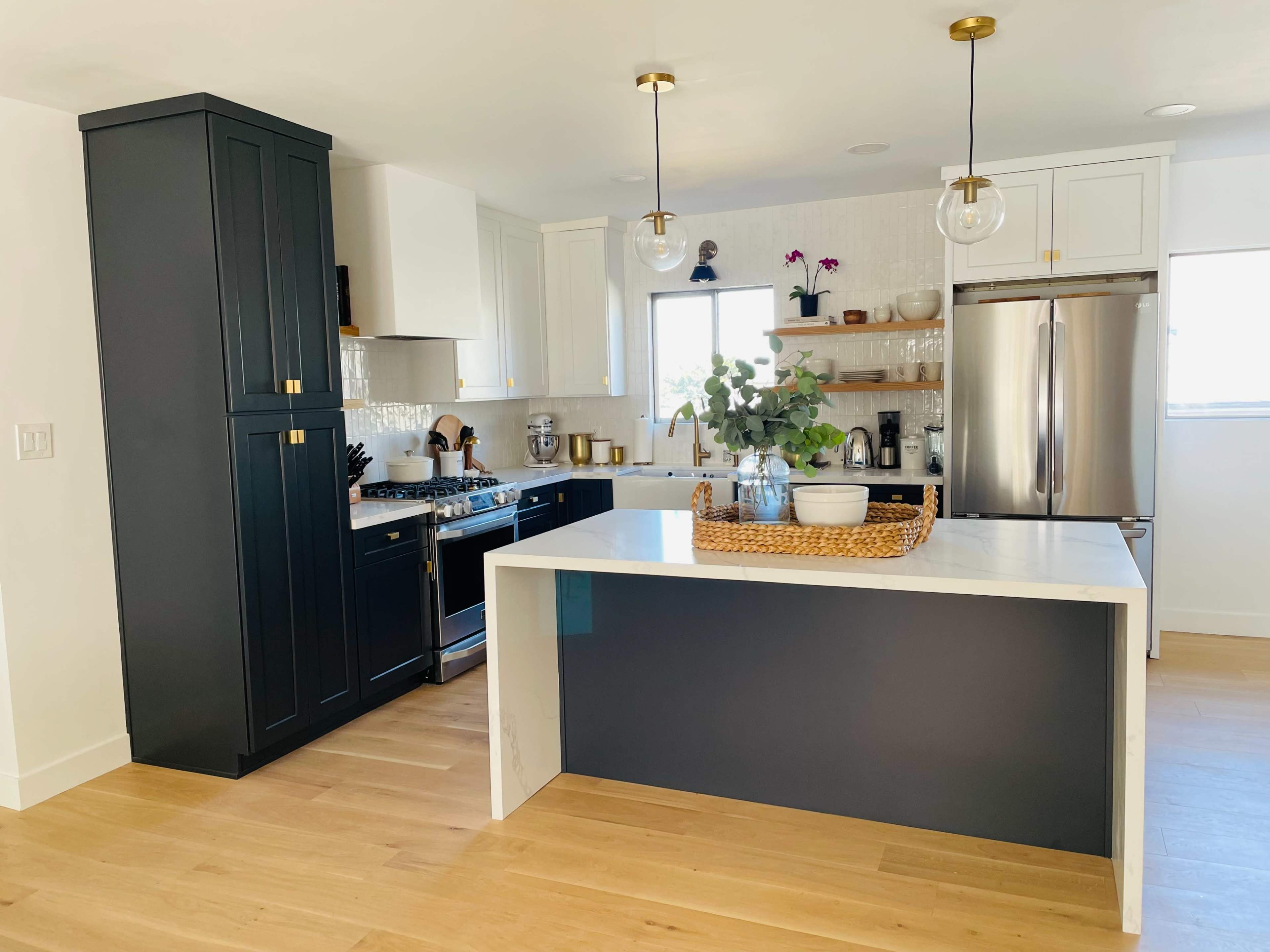 A modern kitchen features dark cabinetry, a bright island, stainless steel appliances, and natural wood flooring.